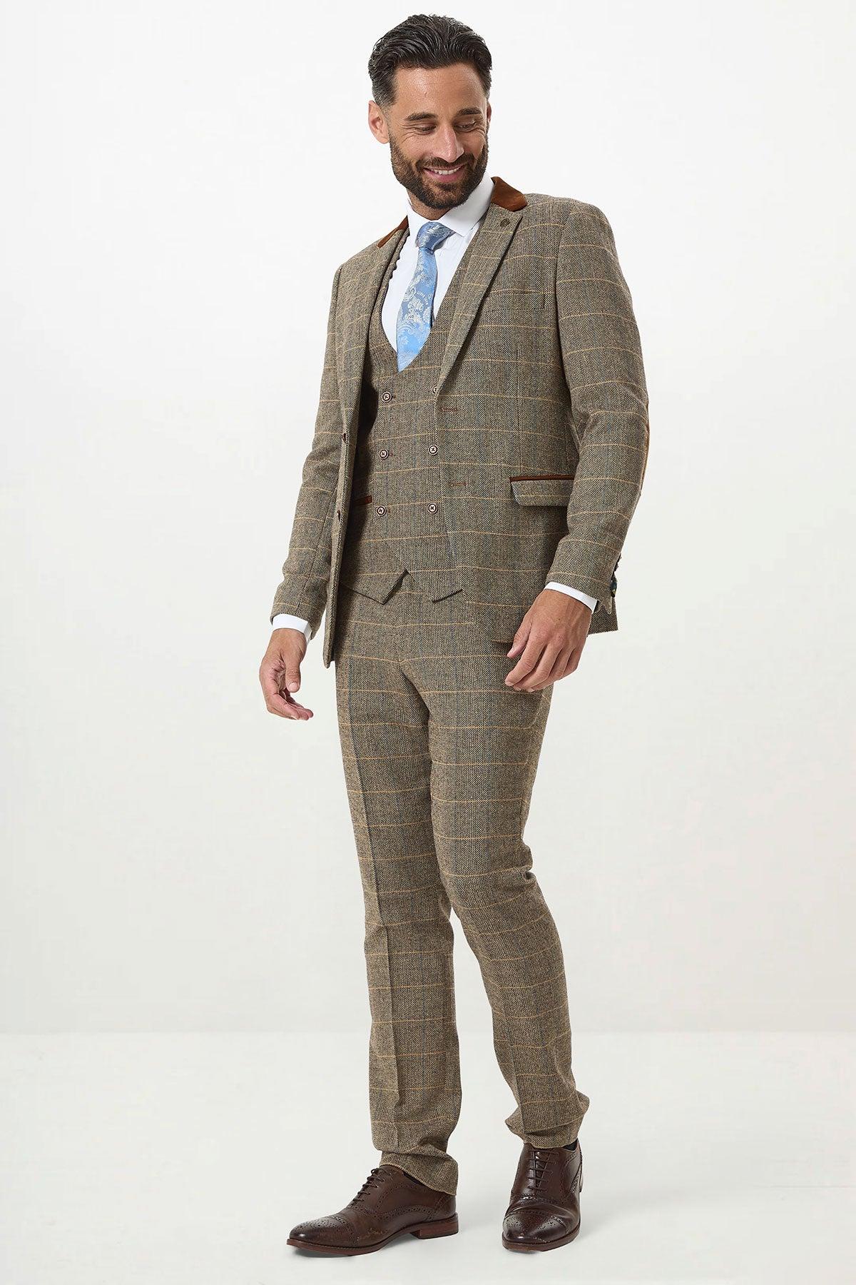 A man wears a marcdarcy DX7 Tan Tweed Check Three Piece Suit with double-breasted waistcoat, white shirt, light blue patterned tie, and brown dress shoes, posing against a white background.