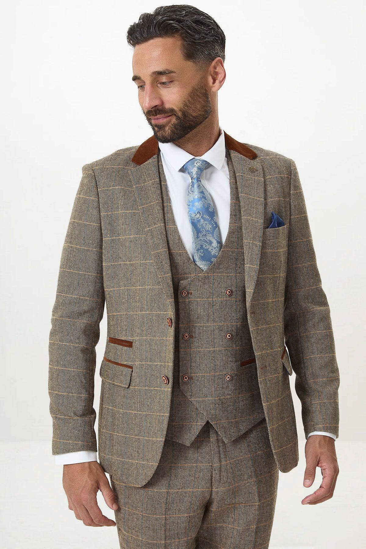 A man with dark hair and a beard is wearing the marcdarcy DX7 Tan Tweed Check Three Piece Suit With Double Breasted Waistcoat, styled with a blue patterned tie and blue pocket square, standing against a plain white background.