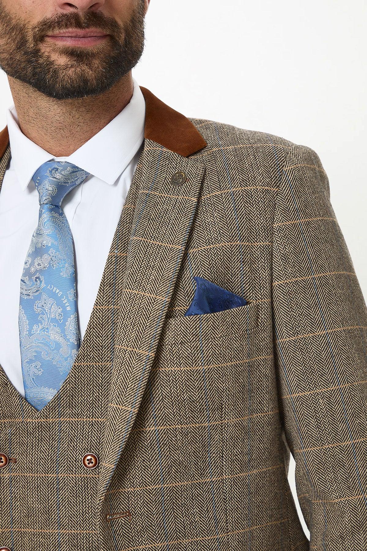A man wearing the marcdarcy DX7 Tan Tweed Check Three Piece Suit with Double Breasted Waistcoat. He pairs it with a white shirt, blue patterned tie, and blue pocket square. Only the lower half of his face and upper body are visible.