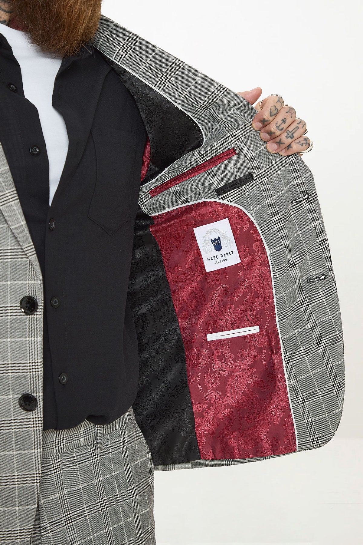 A man wears the Marc Darcy ROSS Grey Check Two Piece Suit with the blazer open, showcasing its red paisley lining and brand label, paired with a black vest.