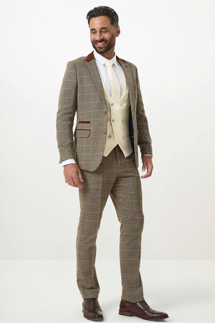 A man smiles in the marcdarcy DX7 Tan Tweed Check Suit with Kelvin Cream Waistcoat, paired with a white shirt, tie, and brown leather shoes. He stands against a plain white background, sporting dark hair and a beard.