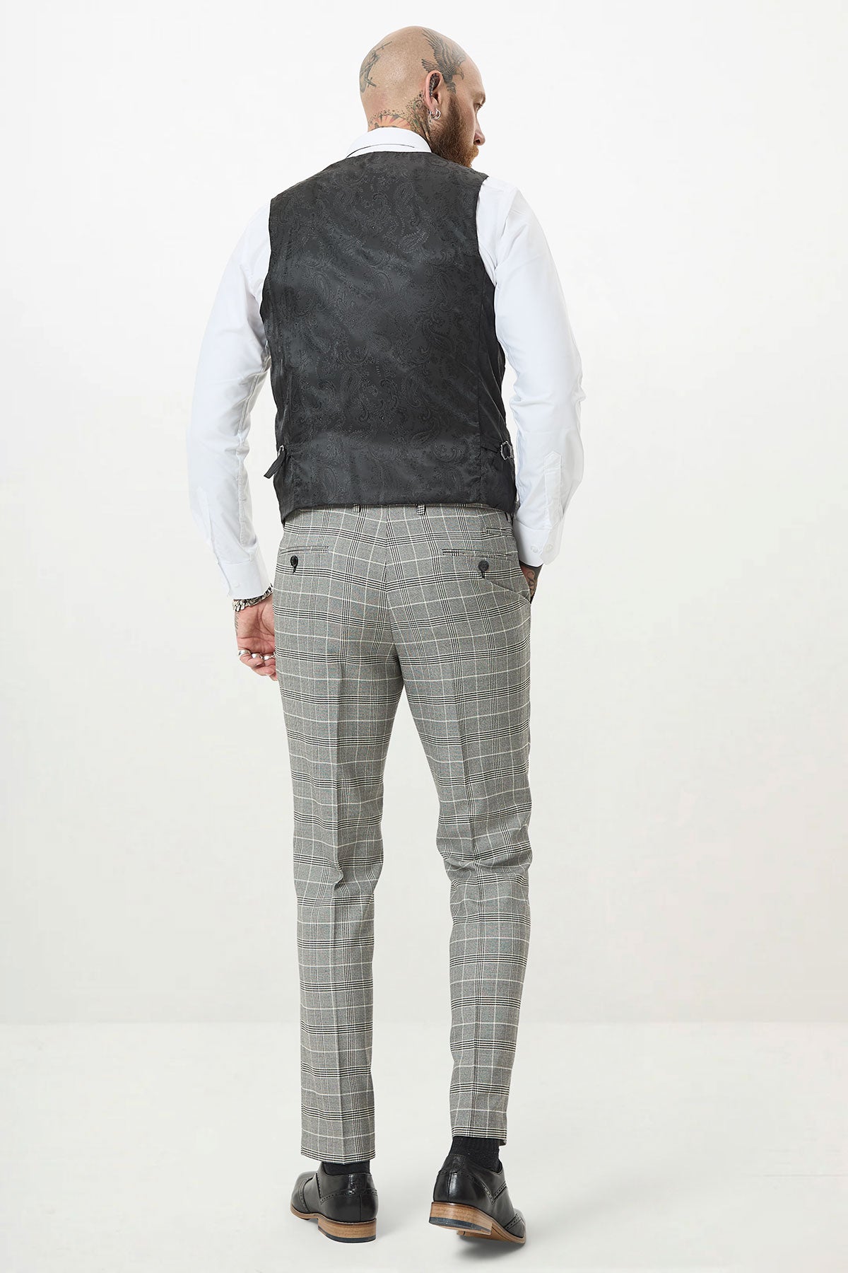 A man with head tattoos stands facing away, wearing the Marc Darcy ROSS Grey Check Three Piece Suit against a plain white background.