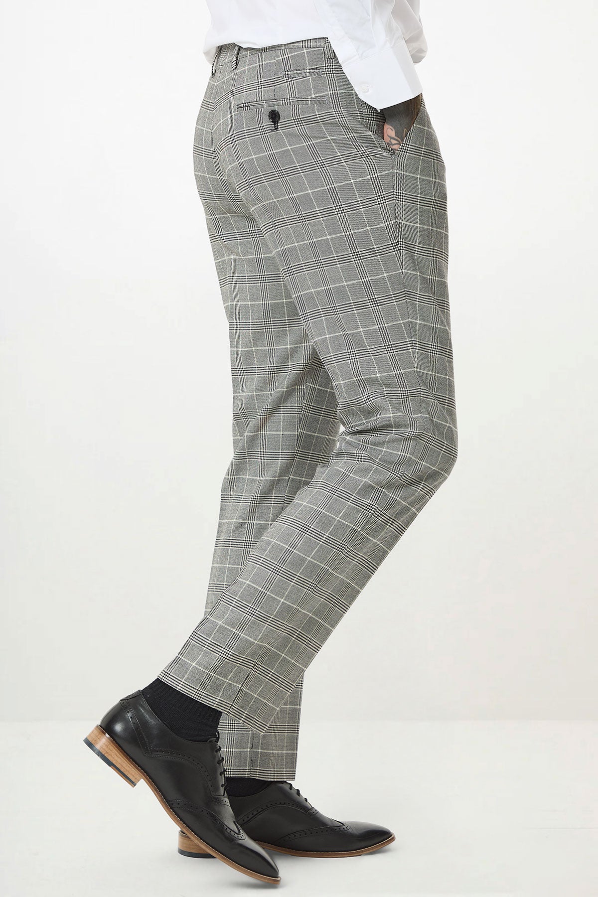A person wearing the Marc Darcy ROSS Grey Check Three Piece Suit with a white shirt and black dress shoes stands sideways, one hand in their pocket, against a plain white background.