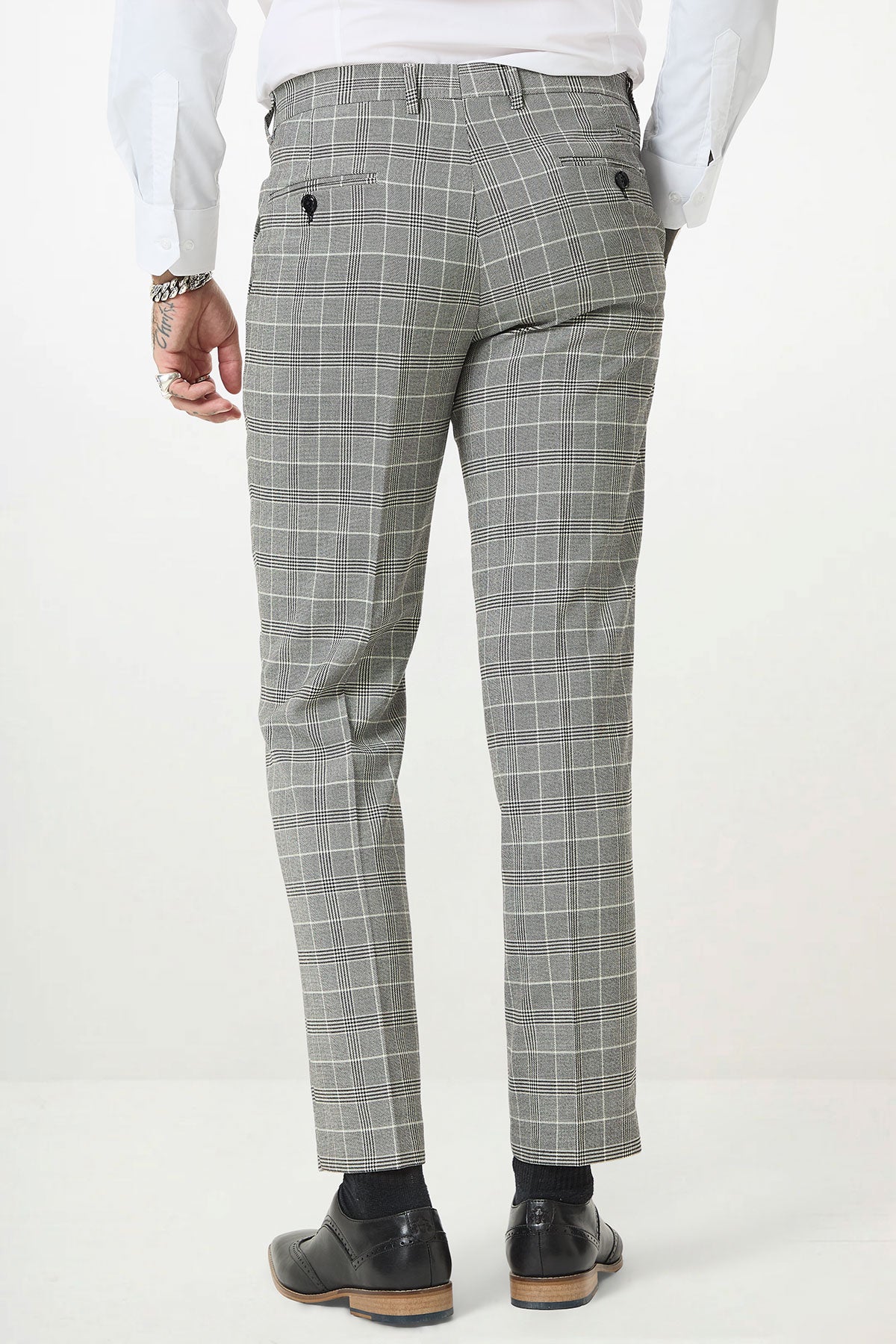A person wearing the Marc Darcy ROSS Grey Check Two Piece Suit, styled with a white shirt, black socks, and black dress shoes, shown from the back against a plain white background.