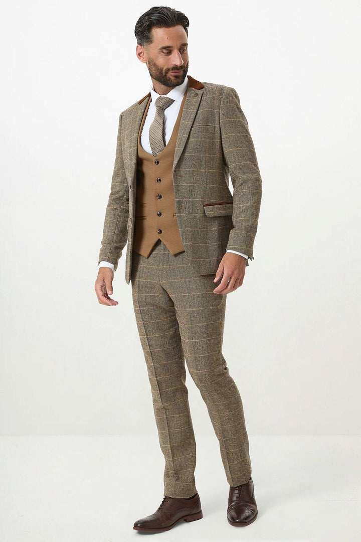 A man wears the marcdarcy DX7 Tan Tweed Check Suit with Kelvin Oak Waistcoat, paired with a white shirt, tie, and brown shoes, posing against a plain white background.