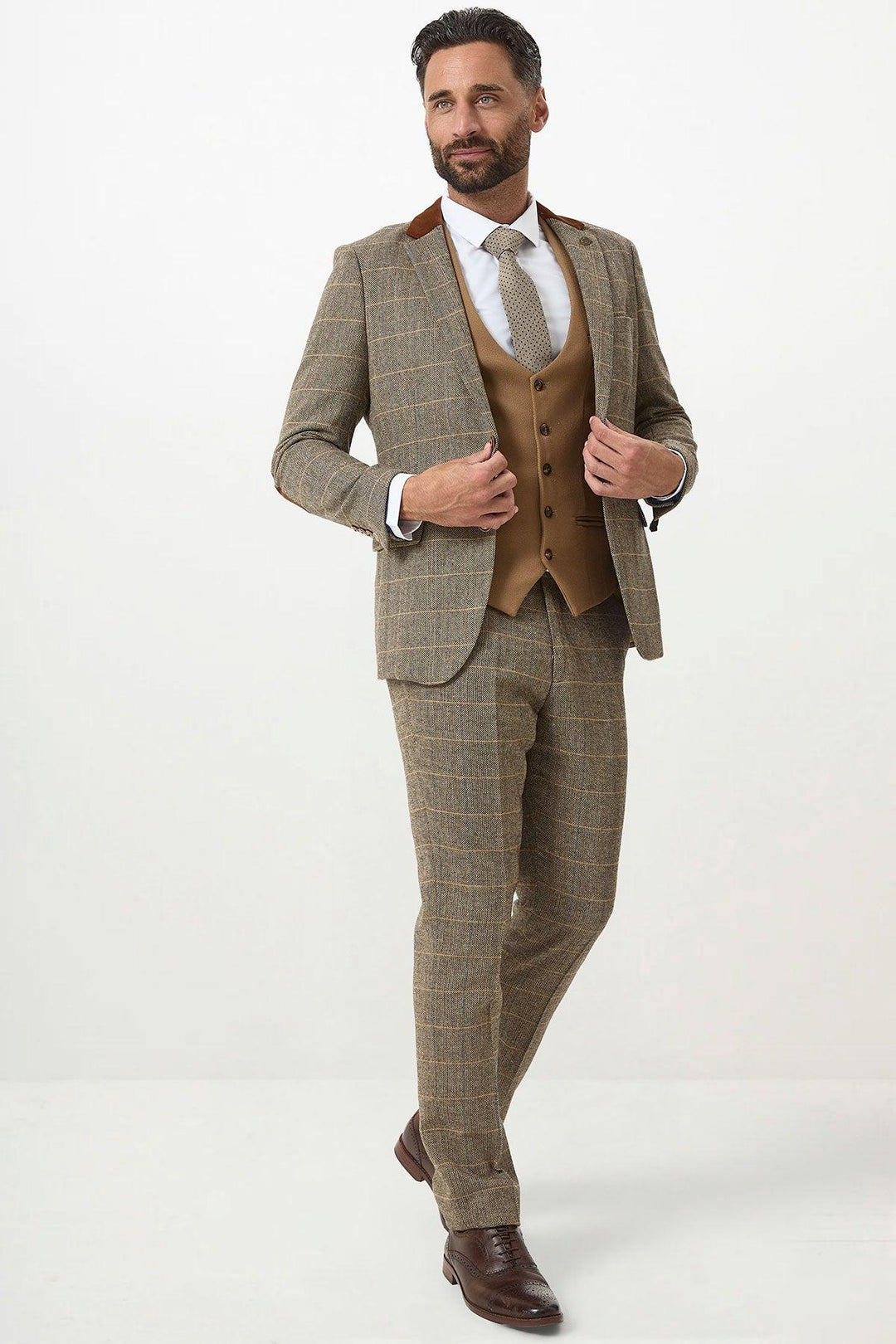 A man with dark hair and a beard models the marcdarcy DX7 Tan Tweed Check Suit with Kelvin Oak Waistcoat, paired with a white shirt and patterned tie. He stands confidently on a plain white background, one hand near his waist.