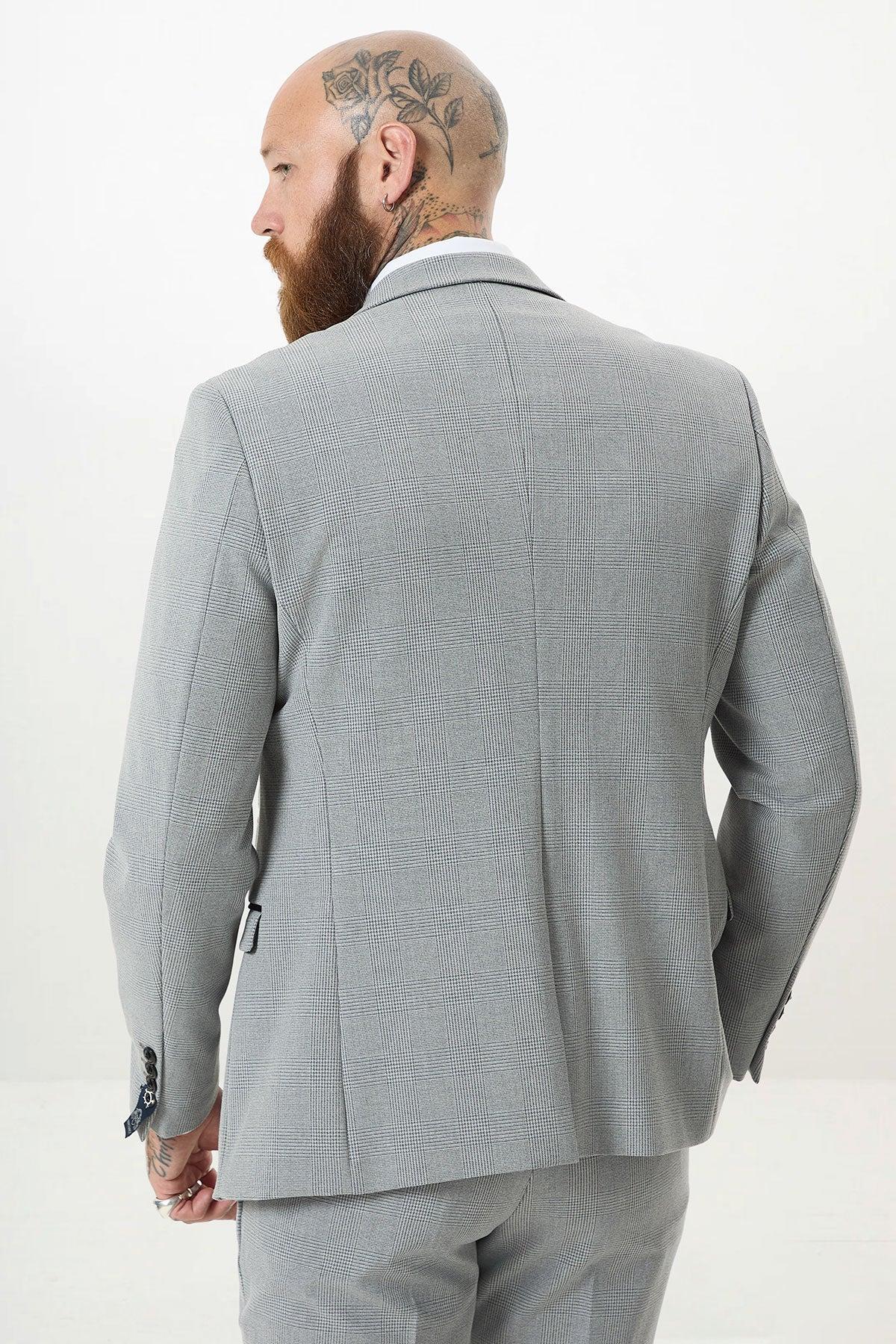 A man with a beard and head tattoos is seen from behind wearing the Marc Darcy BROMLEY Silver Grey Check Three Piece Suit, standing against a plain white background.