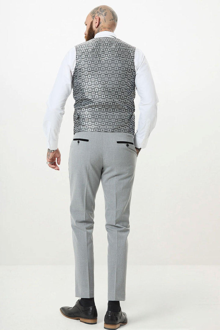 A man with tattoos on his head and hands stands facing away, wearing a white shirt, light gray trousers, black dress shoes, and the Marc Darcy BROMLEY Silver Grey Single Breasted Check Waistcoat.
