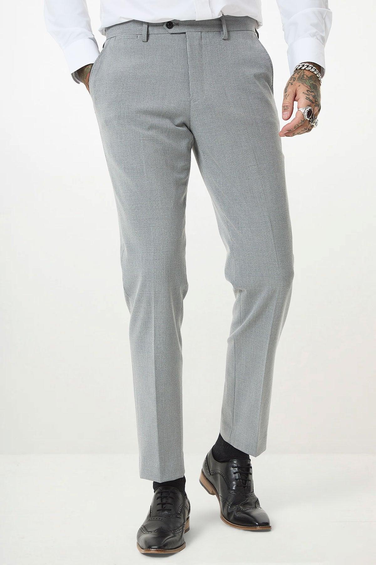 Man wearing the Marc Darcy BROMLEY Silver Grey Check Three Piece Suit, white dress shirt, black socks, and black dress shoes. His tattooed, jewelry-adorned hands are visible by his sides. Image is from chest to feet.