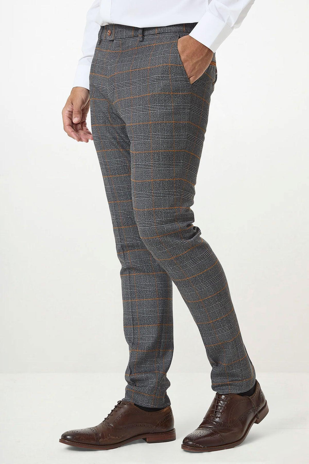 A man wearing marcdarcys JENSON - Grey Check Trousers with an orange check pattern, styled with a white shirt and brown brogue dress shoes, stands against a plain white background.