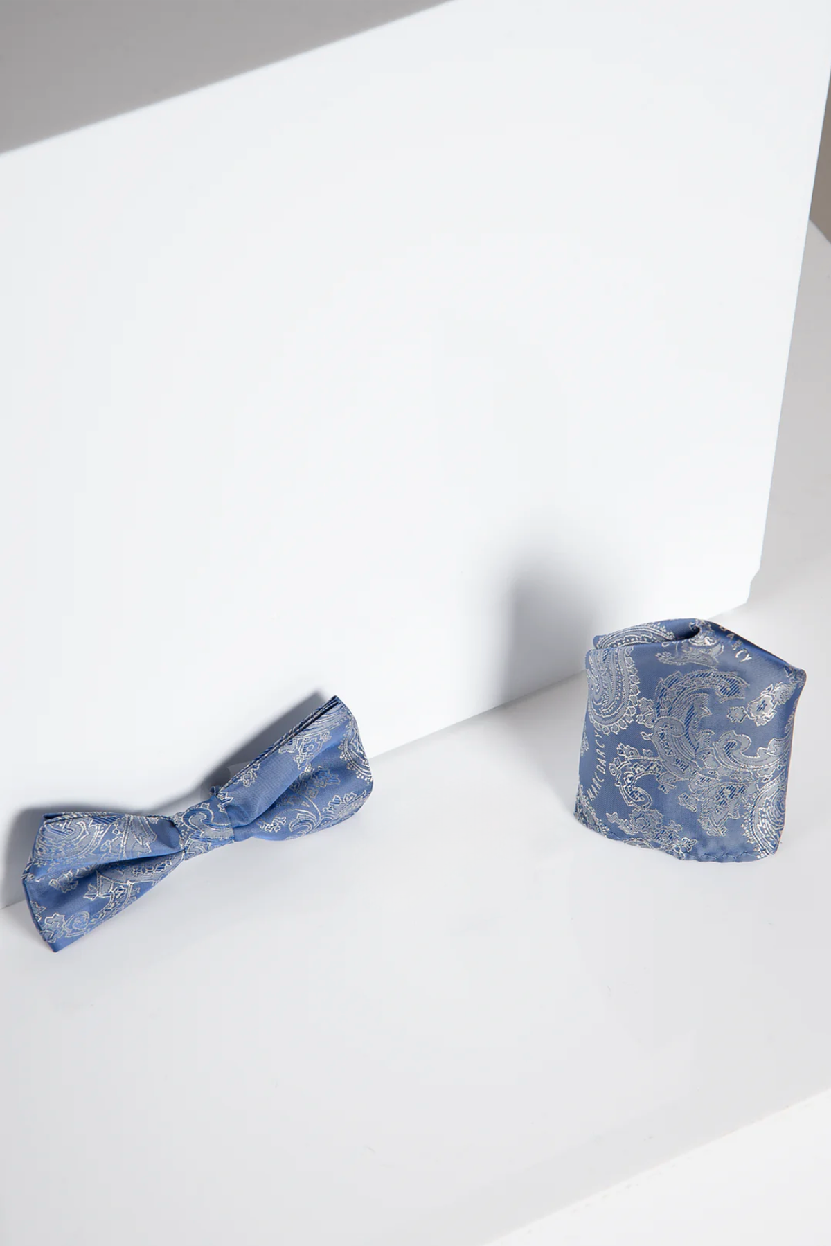 The "MD PAISLEY - Sky Blue Paisley Bow Tie and Pocket Square Set" by Accessory is showcased on a white surface with a minimalistic white background.