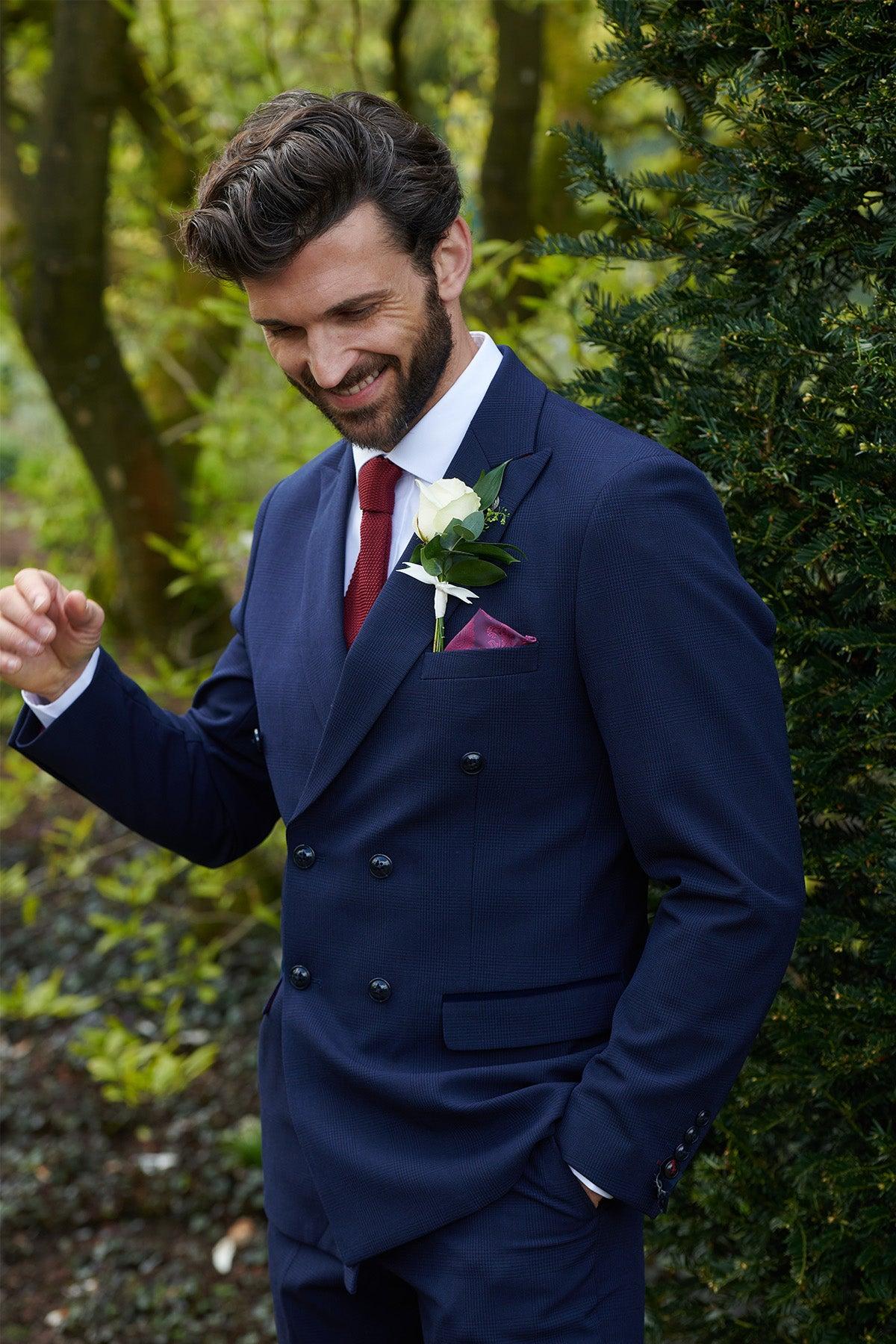A groom in the Marc Darcy BROMLEY Navy Double Breasted Check Blazer smiles as he adjusts his boutonnière and pocket square.