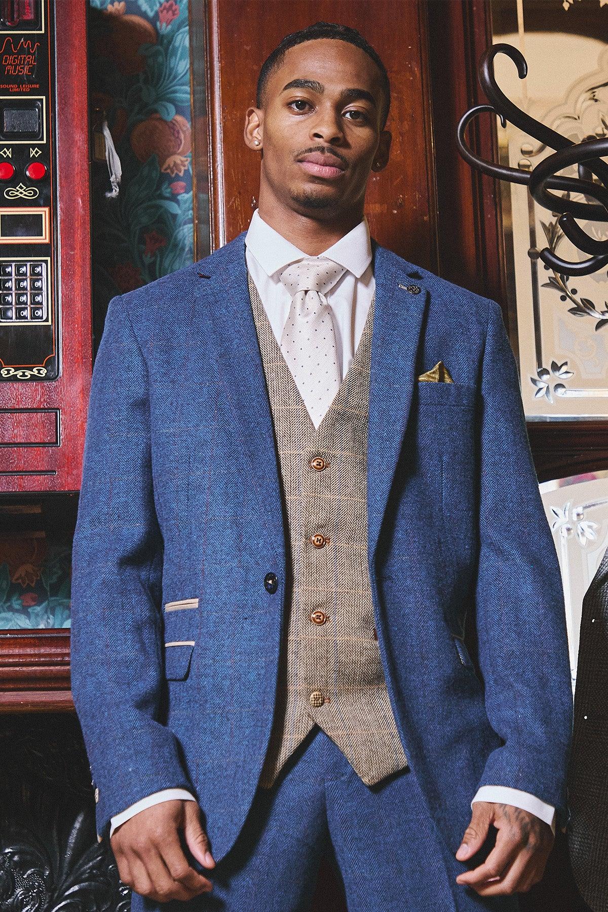 A man poses in the marcdarcy WHU Collection DION Blue Tweed Suit with TED Waistcoat, as worn by Crysencio Summerville, paired with a light pink polka dot tie—an effortlessly sharp look for the modern groom.