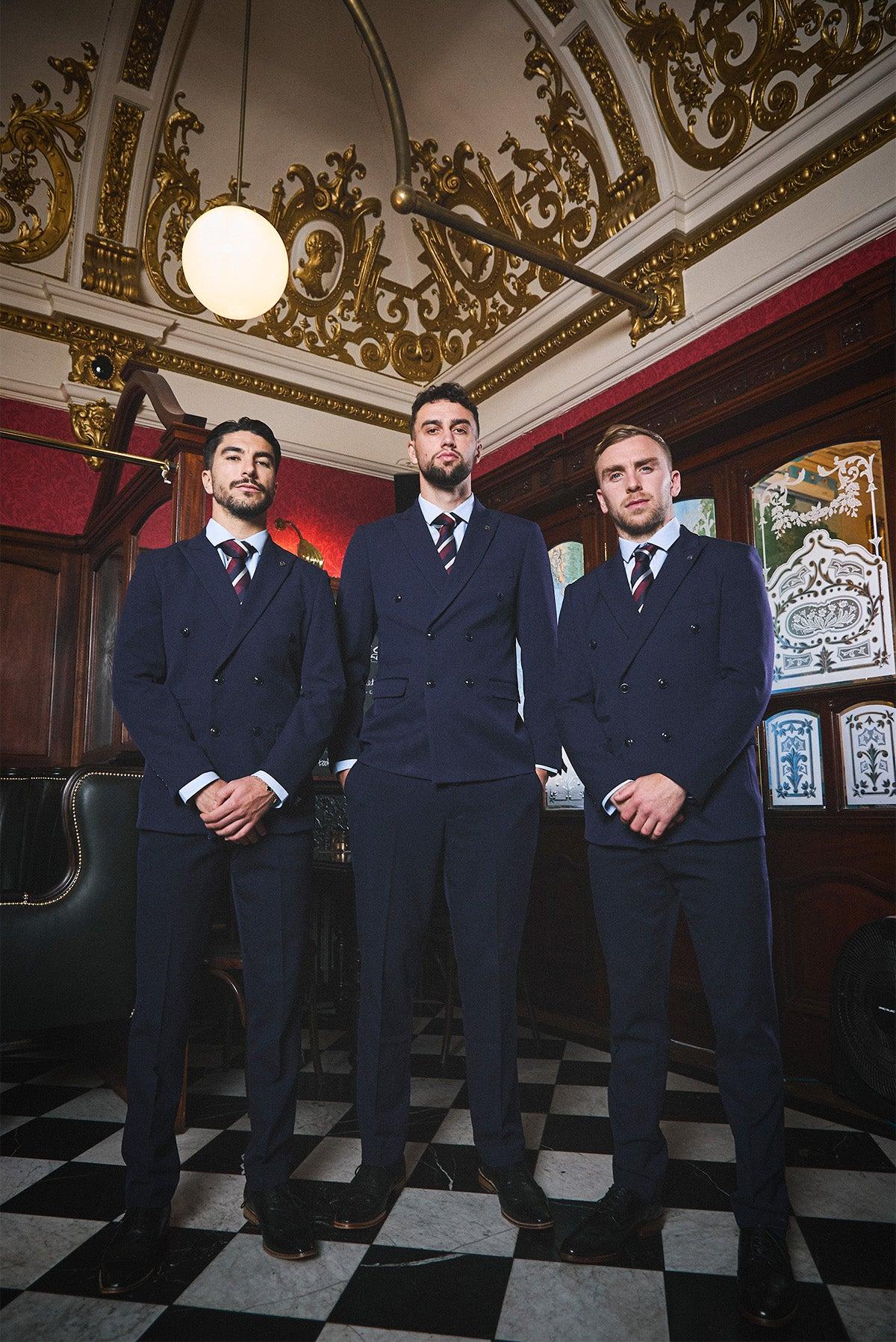 Three men in matching Marc Darcy WHU Collection - BROMLEY Navy Double Breasted Suits, as worn by Jarrod Bowen, pose confidently in an ornate room with gold ceiling, red walls, and a black-and-white checkered floor.