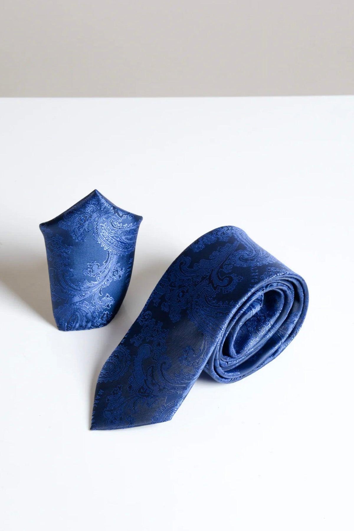 The Accessory MD PAISLEY Midnight Navy Paisley Tie and Pocket Square Set features a folded pocket square and matching rolled tie, both with an elegant paisley design, displayed on a white surface against a light beige background.