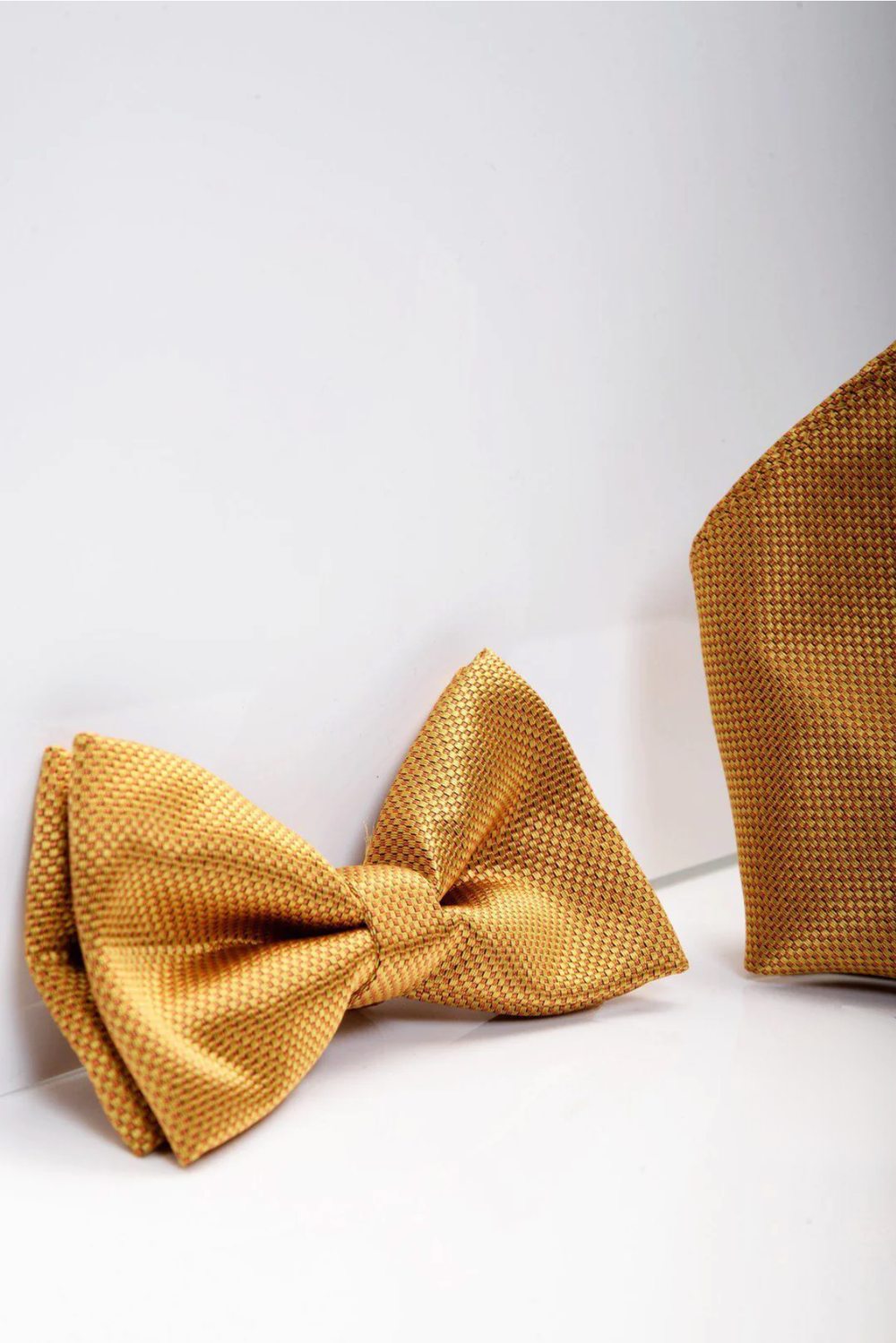 The Accessory TB17 Birdseye Print Bow Tie and Pocket Square Set in Gold is showcased against a white background, emphasizing the elegant birdseye print and sophisticated design of this matching gold set.