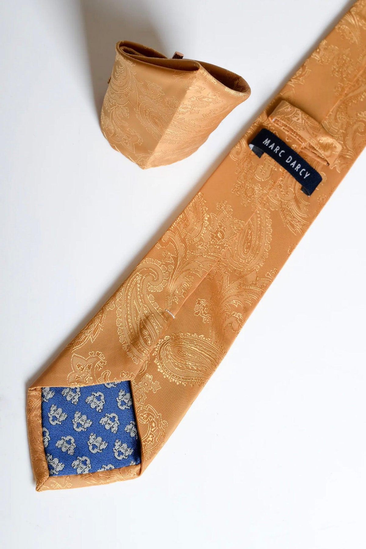 The MD PAISLEY Gold Paisley Tie and Pocket Square Set by Accessory features a blue patterned lining and combines contemporary elegance with refined style, complete with signature detailing.