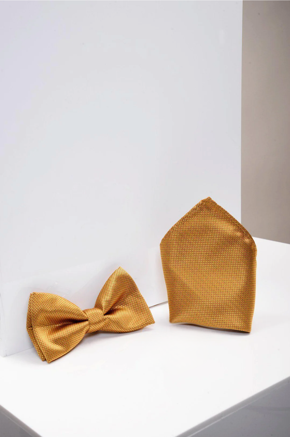 The Accessory TB17 Birdseye Print Bow Tie and Pocket Square Set in Gold is displayed elegantly on a white surface.