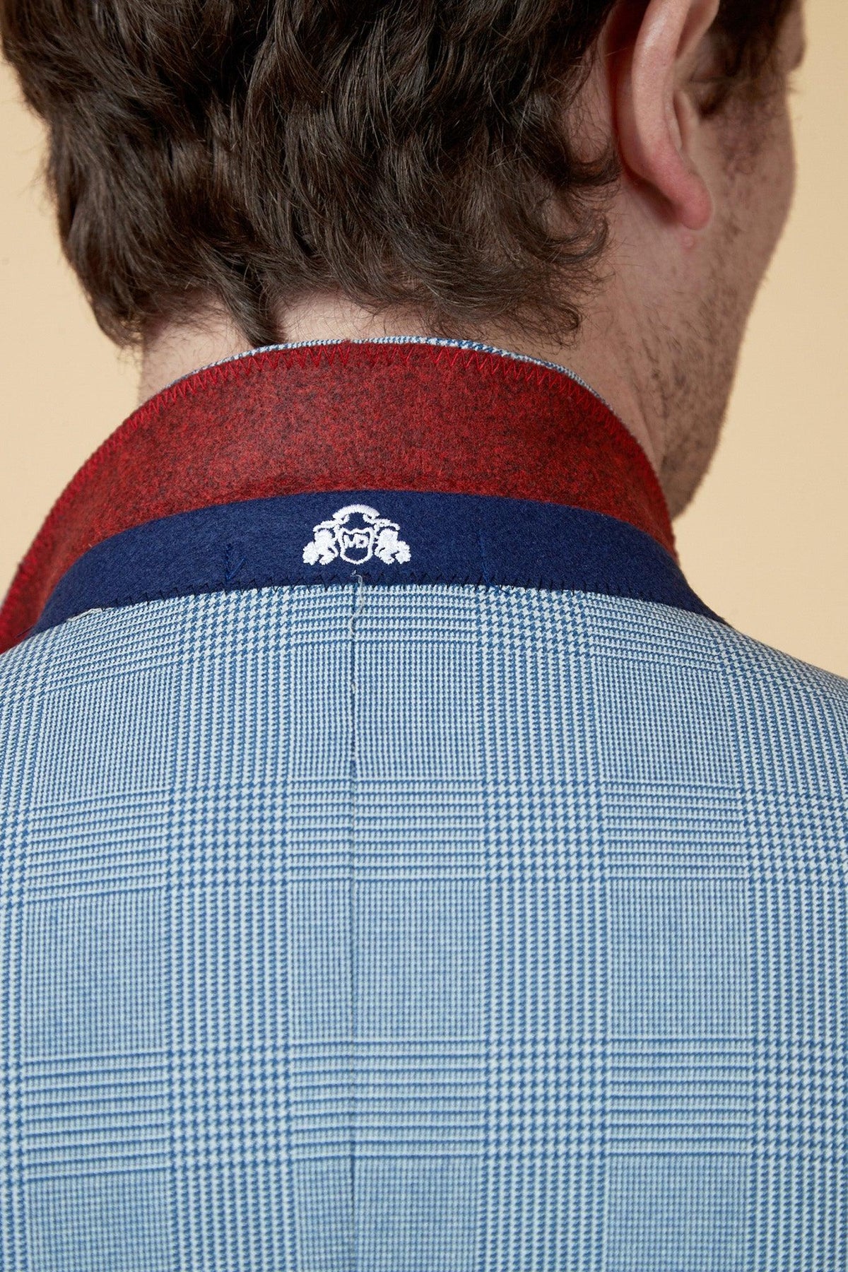 Close-up of a short-haired person wearing the Marc Darcy WBA Collection - BROMLEY Suit, featuring a Prince of Wales check with red and navy collar and white crest logo, as worn by Brandon Thomas-Asante.
