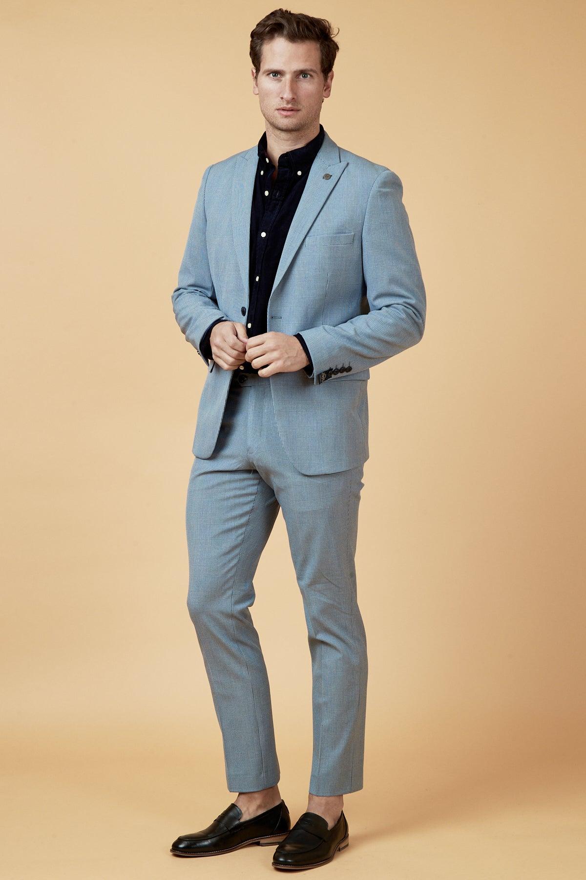 Coronation Street’s Joel Deering (Calum Lill) wears a Marc Darcy BROMLEY Sky Blue Blazer with wine chinos, standing against a beige background.