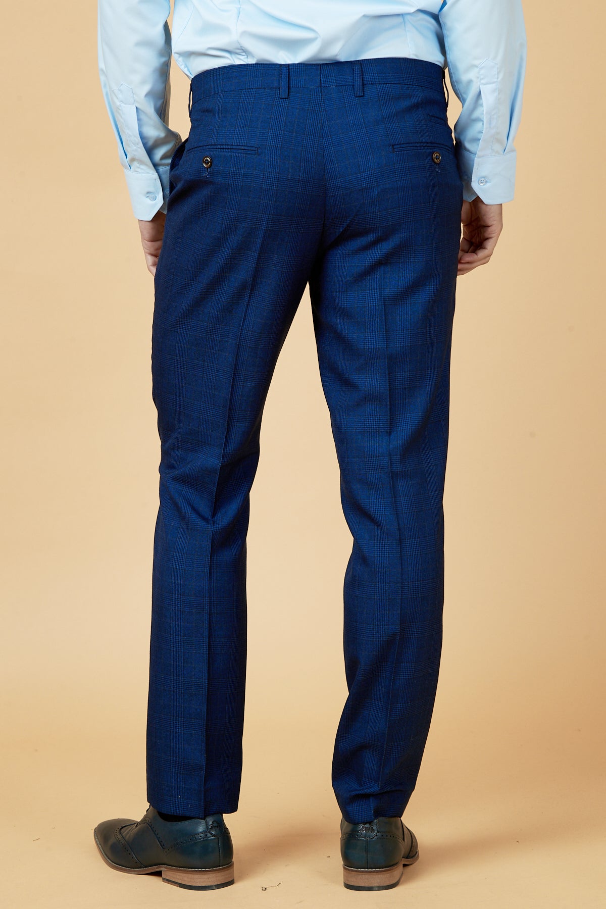 Back view of a man in marcdarcy GEORGE - Royal Blue Check Trousers featuring button welt pockets, styled with a light blue dress shirt and dark oxford shoes—ideal men's work trousers for the office.