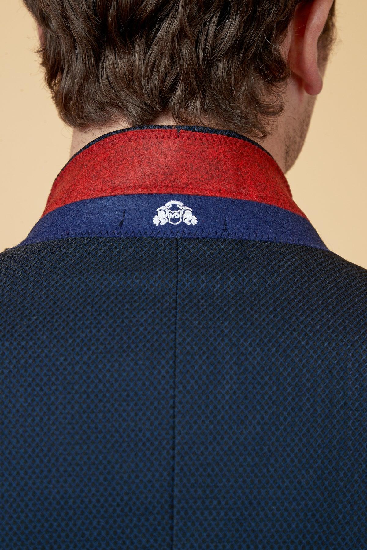 A close-up of the back of Dwight McNeil in The Everton Collection Max Navy Suit by marcdarcy, showing a red and blue collar with a small white embroidered crest. His brown hair highlights the sharp, slim fit style.