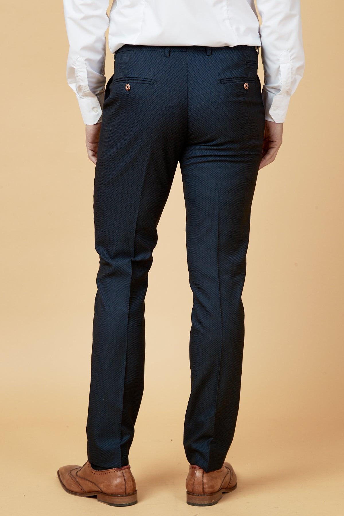Dwight McNeil, dressed in marcdarcy's The Everton Collection Max Navy Suit pants and a white shirt, is seen from the back in front of a plain beige background.