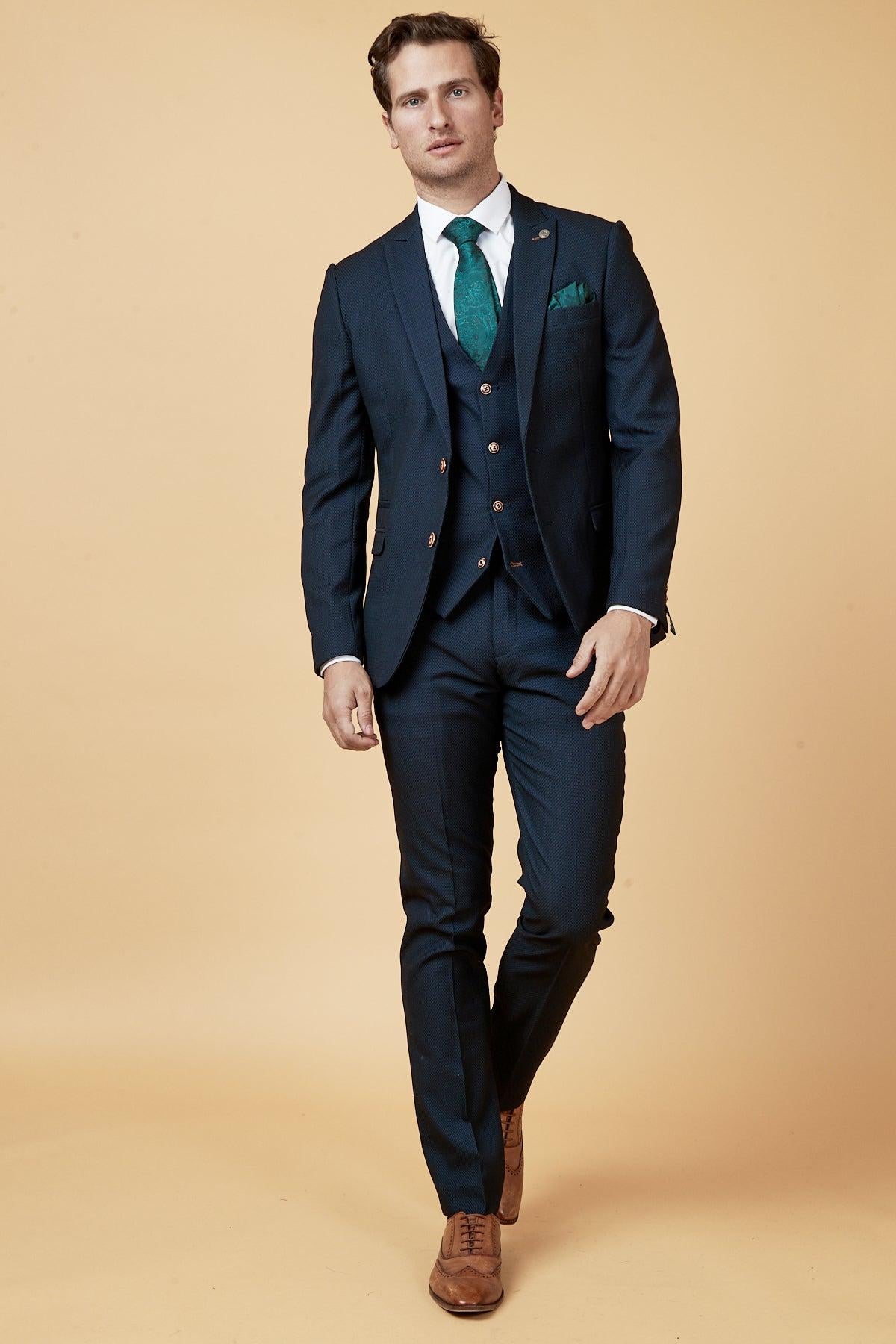 Dwight McNeil wears the marcdarcy Everton Collection Max Navy suit with a vest, white shirt, green paisley tie, and brown shoes.