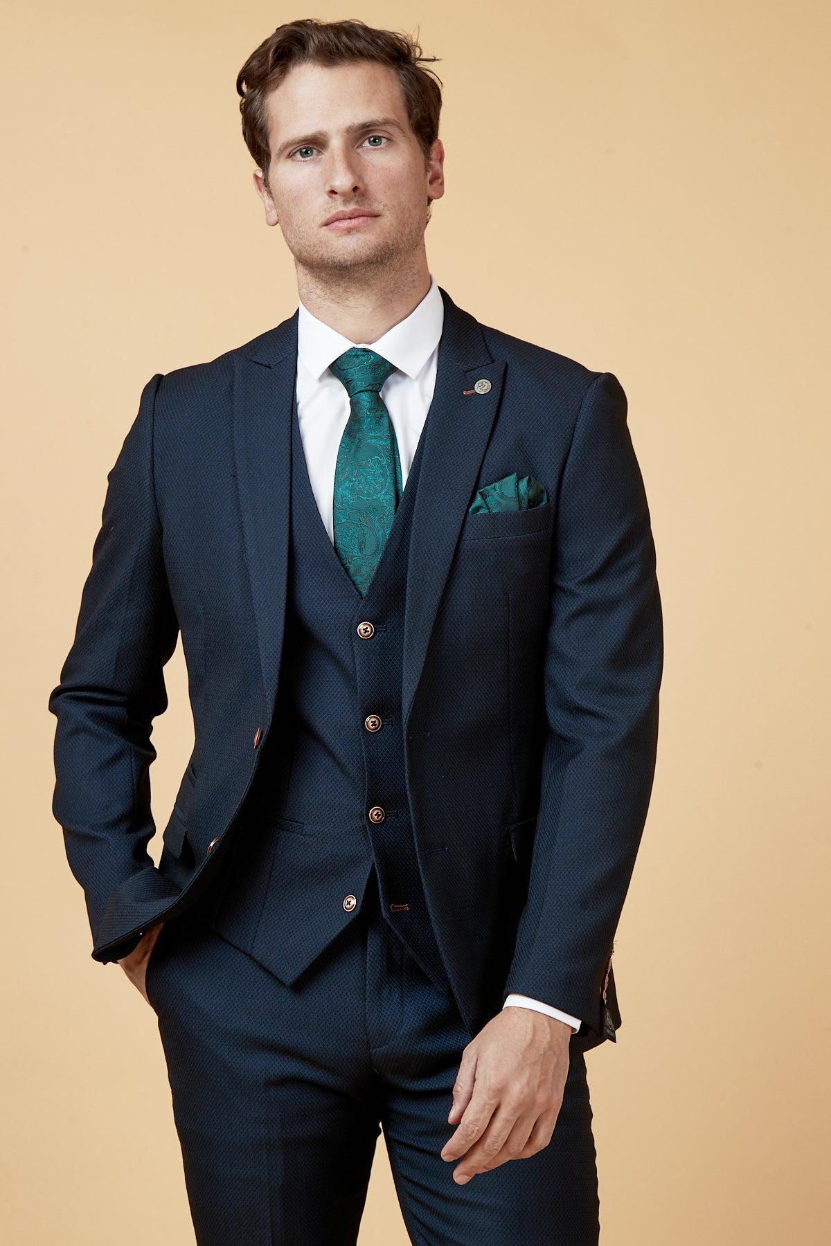 A man models The Everton Collection | Dwight McNeil In Max Navy Suit by marcdarcy, styled with a matching waistcoat, crisp white shirt, teal paisley tie, and pocket square.