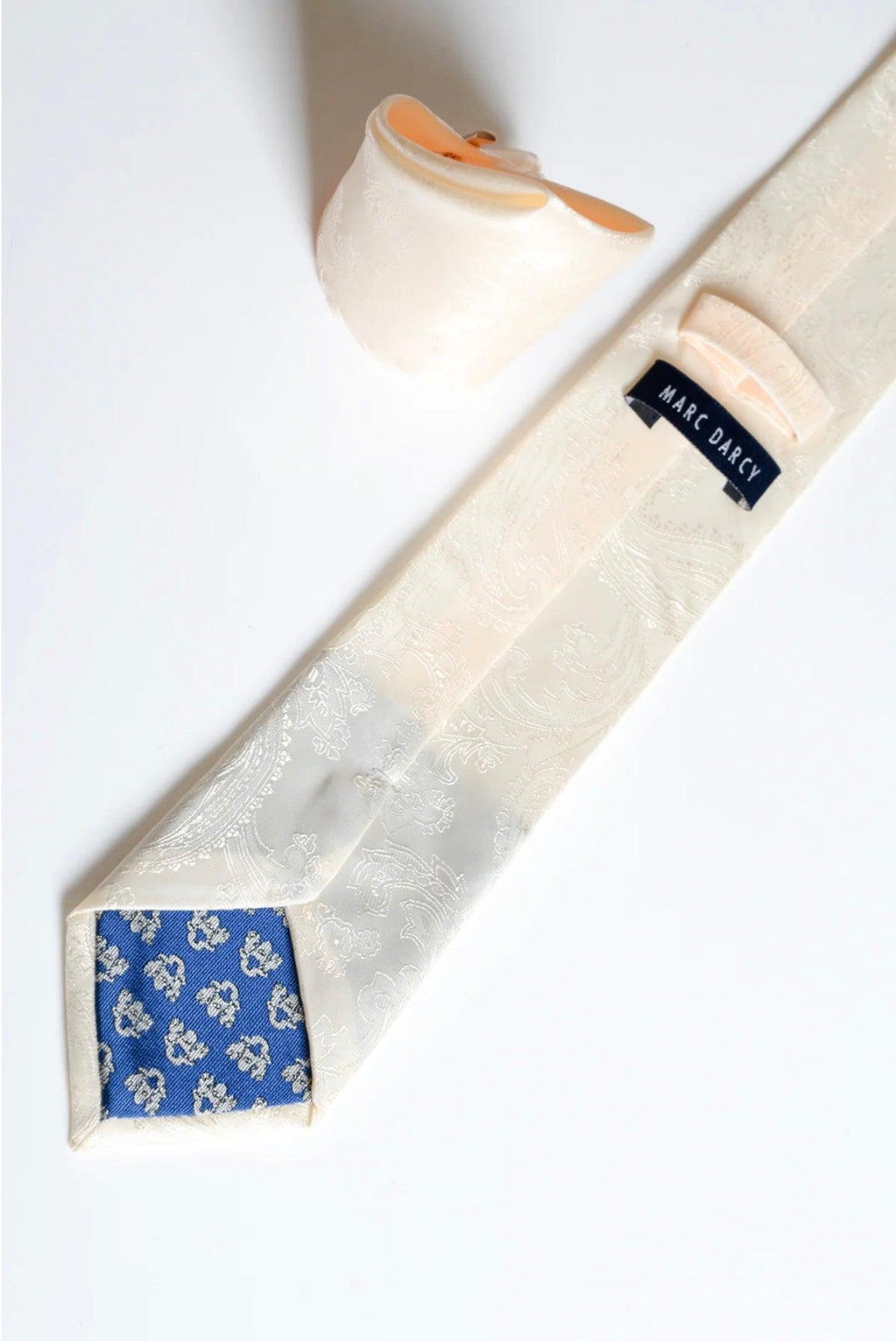 The MD PAISLEY Cream Paisley Tie and Pocket Square Set by Accessory features a cream paisley tie with blue floral tip lining and a matching pocket square, elegantly shown on a white background.