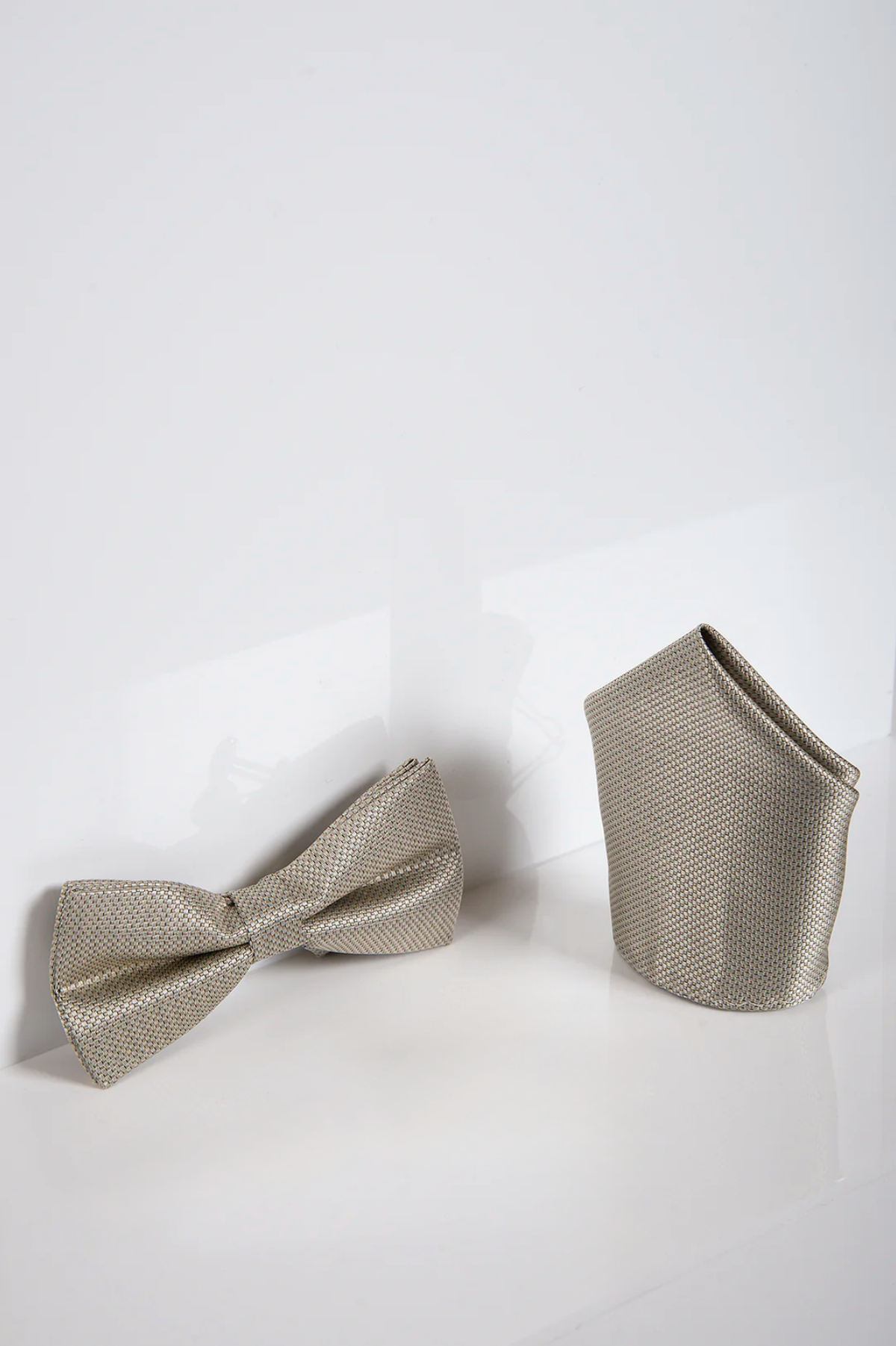The Accessory TB17 Birdseye Print Bow Tie and Pocket Square Set in Tan is shown on a glossy white surface against a plain backdrop, offering a sophisticated and stylish accessory duo.