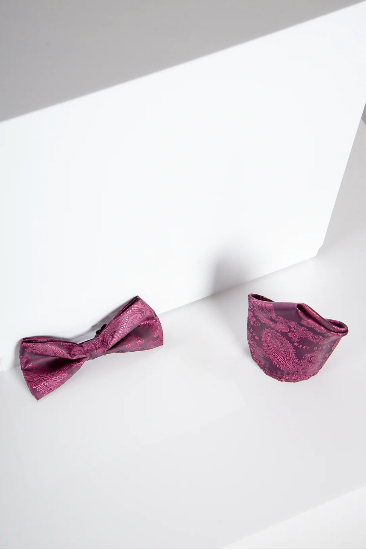 The Accessory MD PAISLEY - Berry Paisley Bow Tie and Pocket Square Set is displayed on a white surface with a white geometric background.