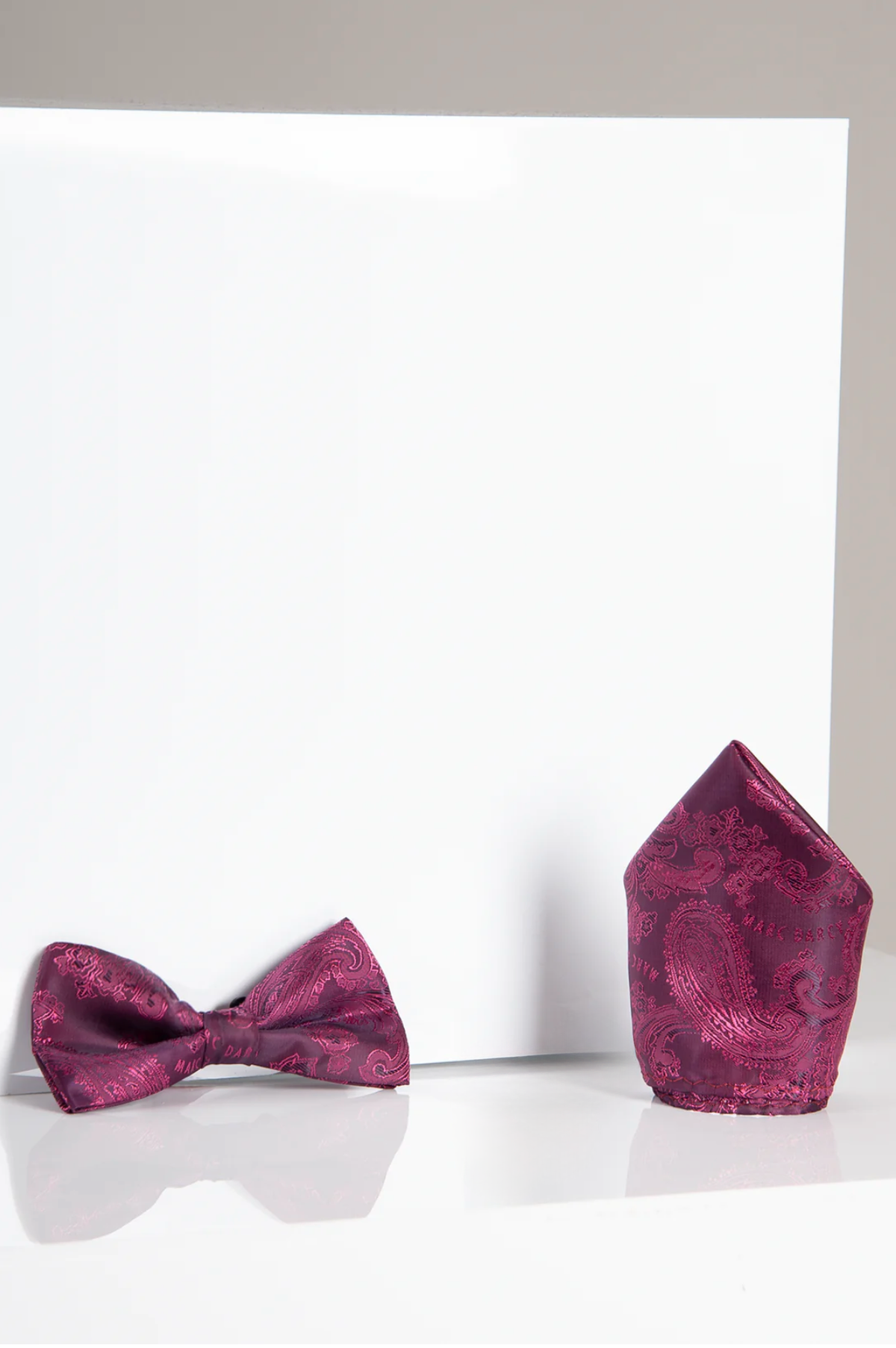 The Accessory MD PAISLEY - Berry Paisley Bow Tie and Pocket Square Set is shown on a white surface, featuring a stylish dark pink paisley design.