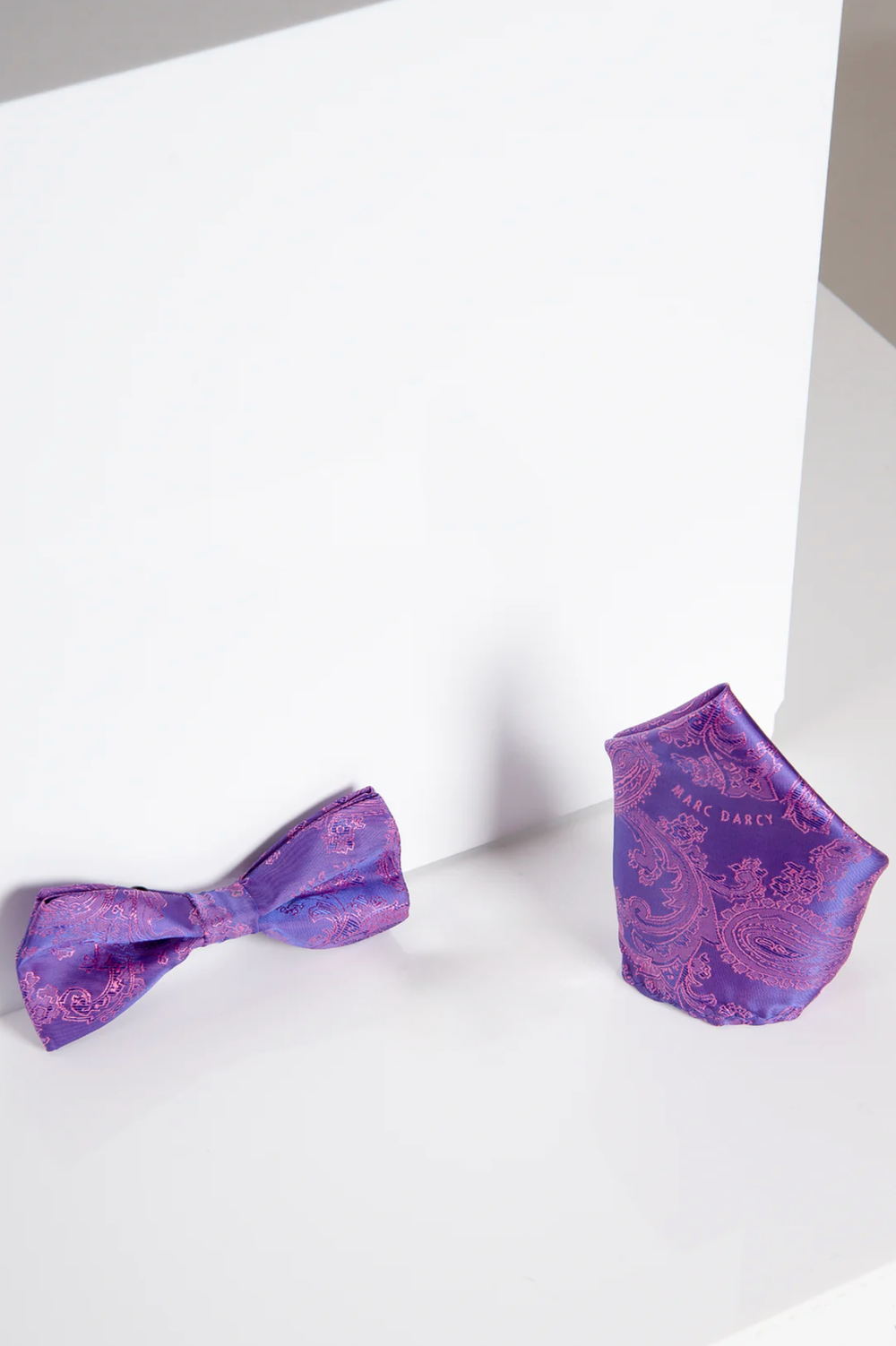 The Accessory MD PAISLEY - Purple Paisley Bow Tie and Pocket Square Set is displayed upright on a white surface, with the stylish bow tie and matching pocket square shown against a plain white background.