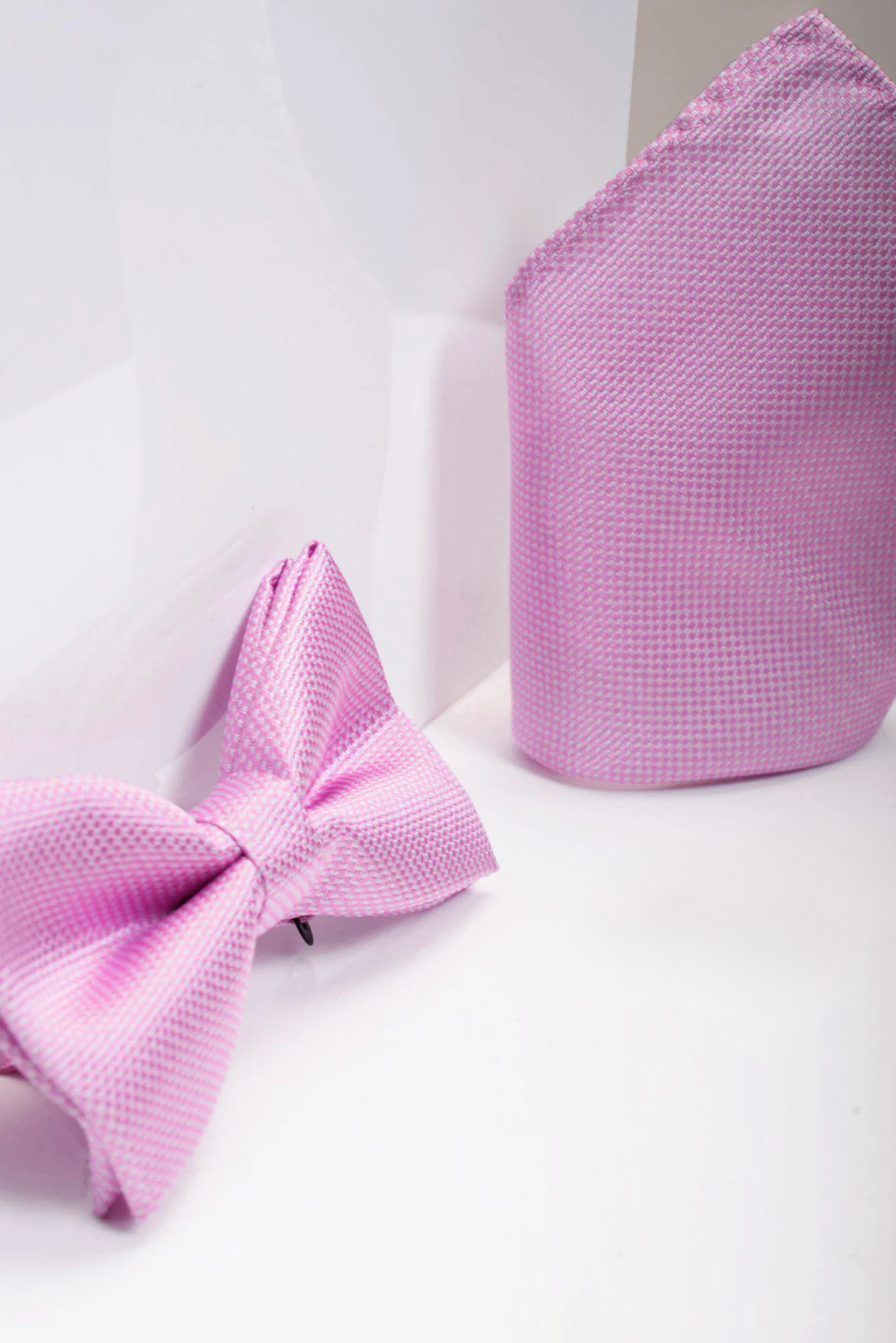 A close-up of the TB17 Birdseye Print Bow Tie and Pocket Square Set in Pink by Accessory, neatly arranged on a white background—a stylish wedding accessory option.