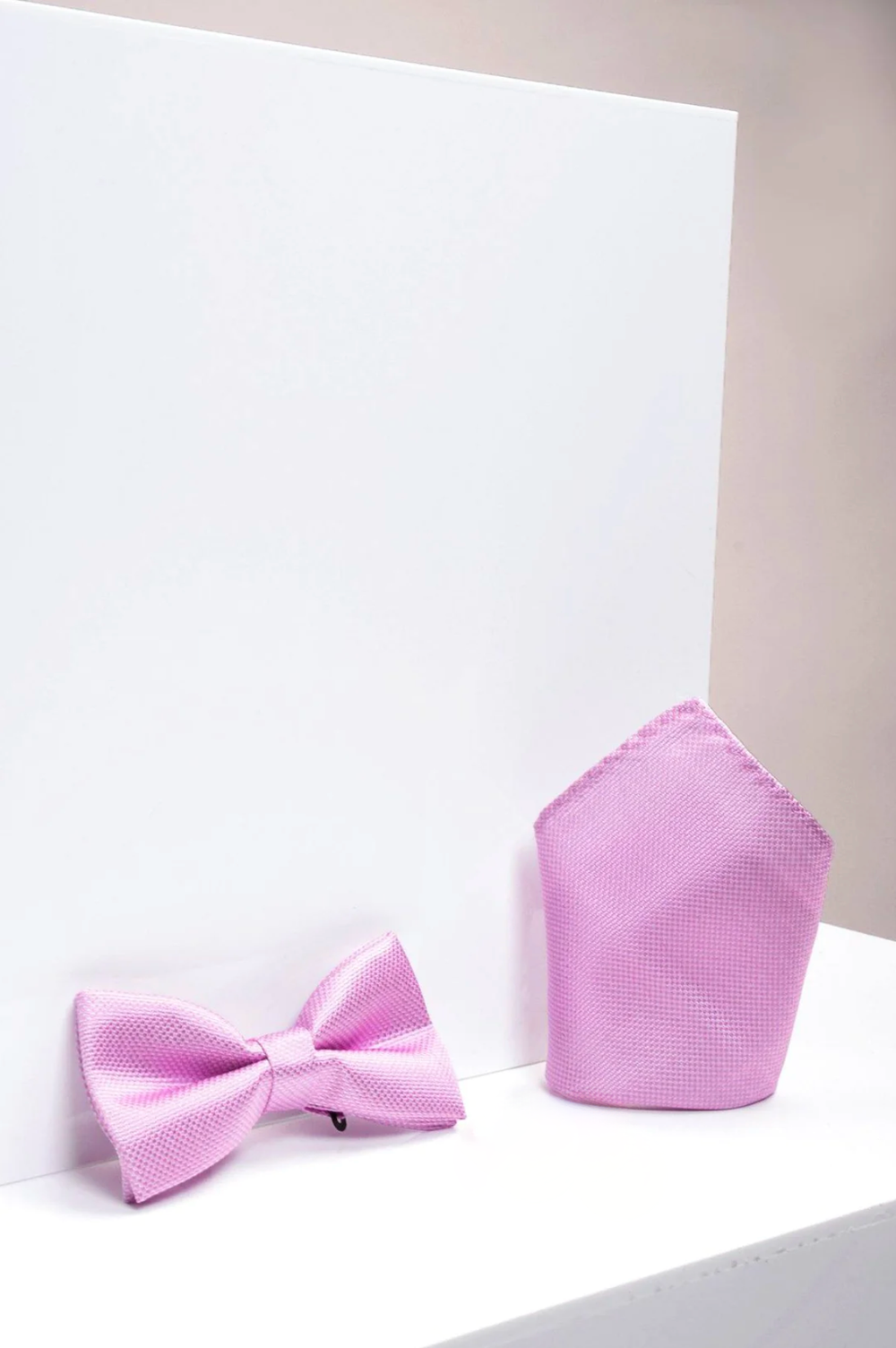 The TB17 - Birdseye Print Bow Tie and Pocket Square Set in Pink by Accessory is shown side by side on a white background with soft lighting—an elegant wedding accessory.