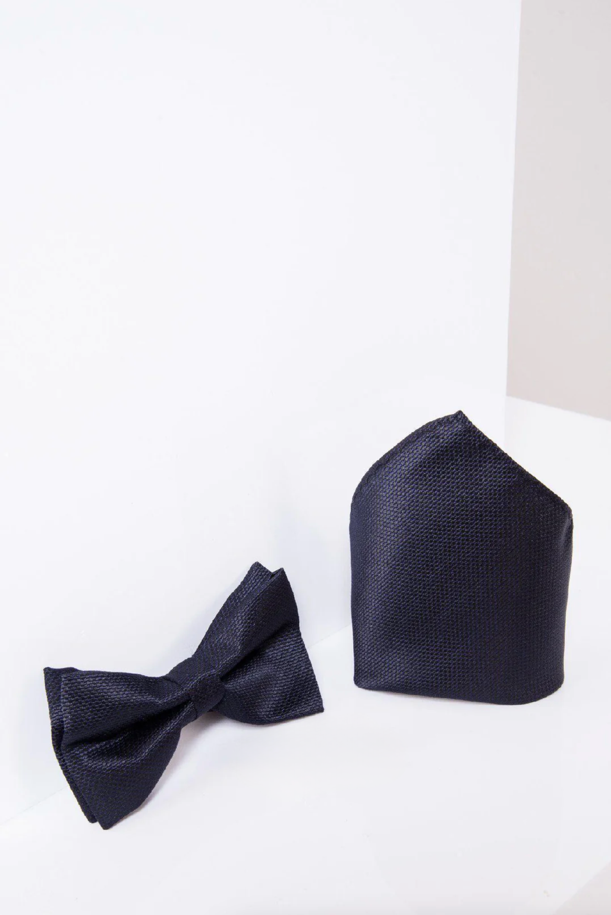 The Accessory TB17 Birdseye Print Bow Tie and Pocket Square Set in Midnight is shown on a white surface with a seamless white background.