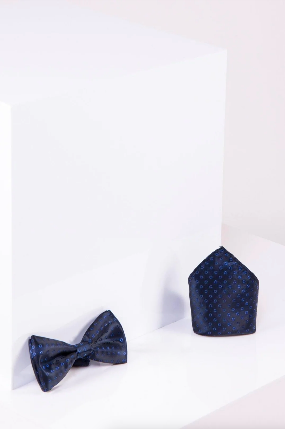 The Accessory BT TUBES - Navy Spot Bow Tie and Pocket Square Set is shown on a white surface before a white cube.