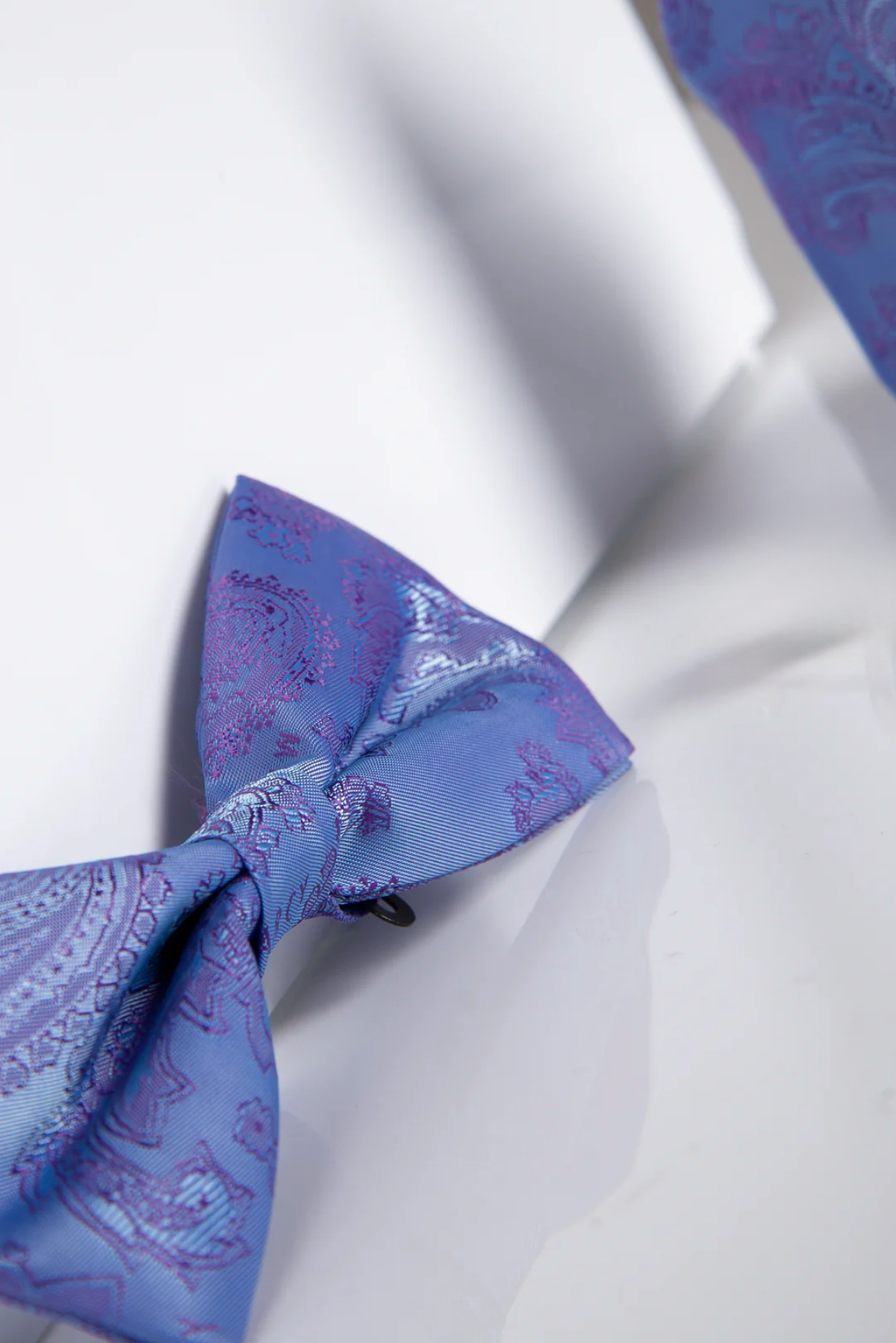 The Accessory MD PAISLEY Lilac Paisley Bow Tie and Pocket Square Set features a blue and purple paisley design on a white background—ideal for enhancing your look with coordinated style.