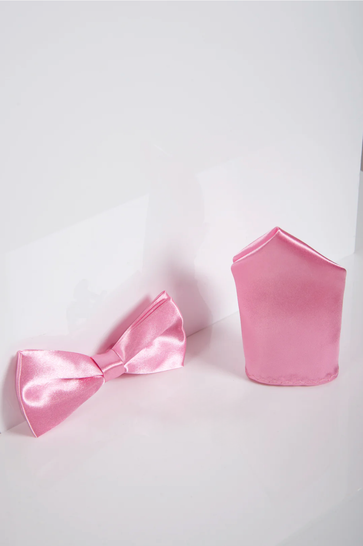 The Accessory SB - Satin Bow Tie and Pocket Square Set In Pink is shown side by side against a white background, featuring a shiny pink satin bow tie with a matching satin pocket square.