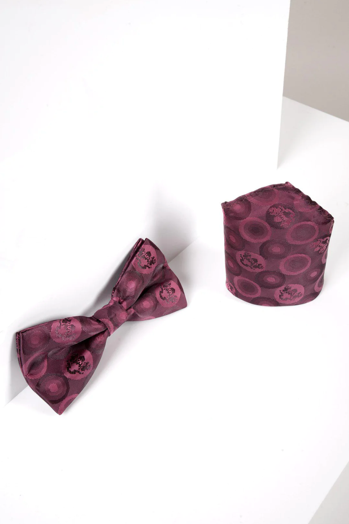The Marc Darcy BUBBLES - Berry Bubble Circle Print Bow Tie and Pocket Square Set features a berry-toned circular pattern, elegantly displayed on a white surface with angled shadows.