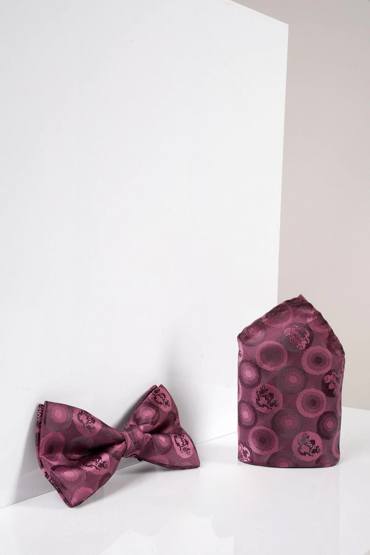 The Marc Darcy BUBBLES - Berry Bubble Circle Print Bow Tie and Pocket Square Set is shown in berry with a circular pattern against a white and light gray background.