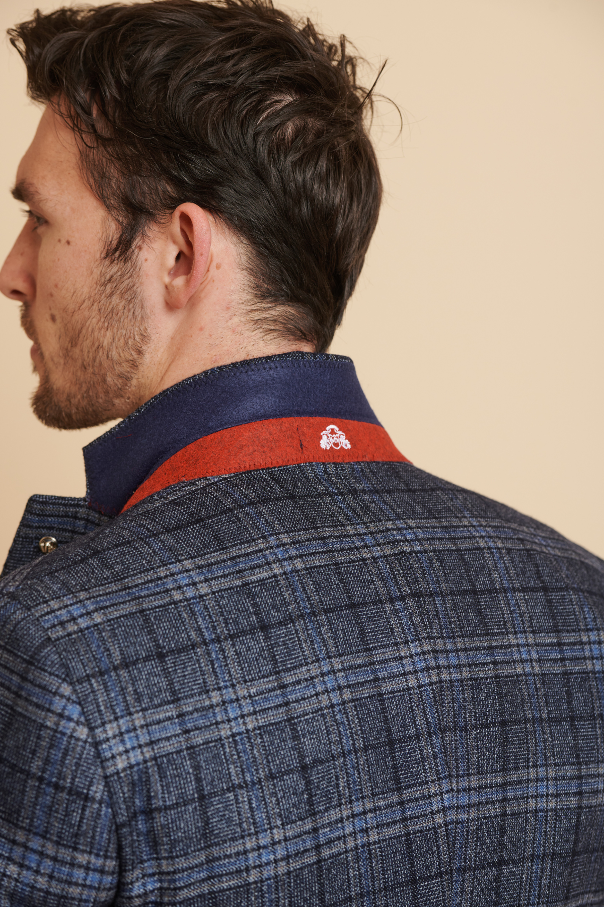 A man with short dark hair is seen from behind, wearing the Marc Darcy ANDY - Blue Check Three Piece Suit, collar turned up to reveal a contrasting blue and red lining with a small white logo on the red strip.