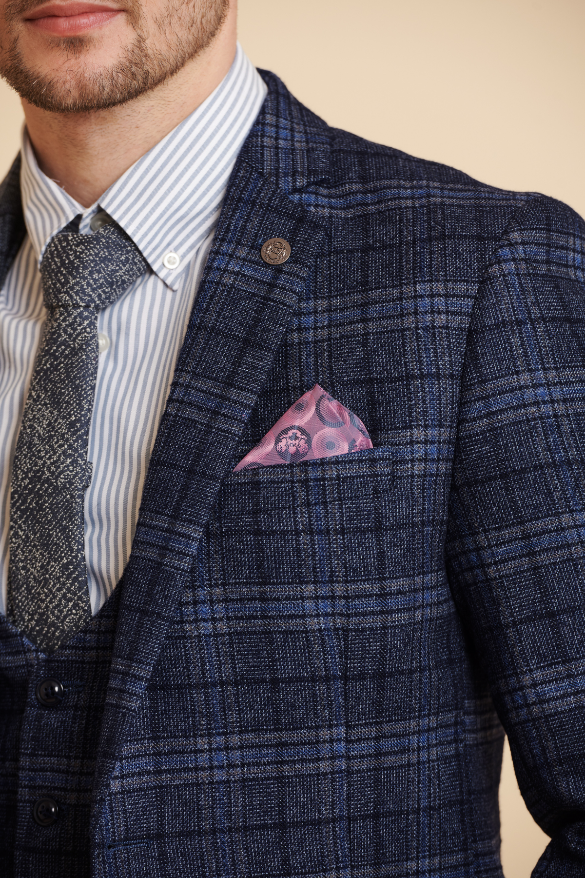 Close-up of a man wearing the ANDY - Blue Check Blazer by Marc Darcy, paired with a striped shirt, textured tie, and pink patterned pocket square for a modern spin on classic formalwear.