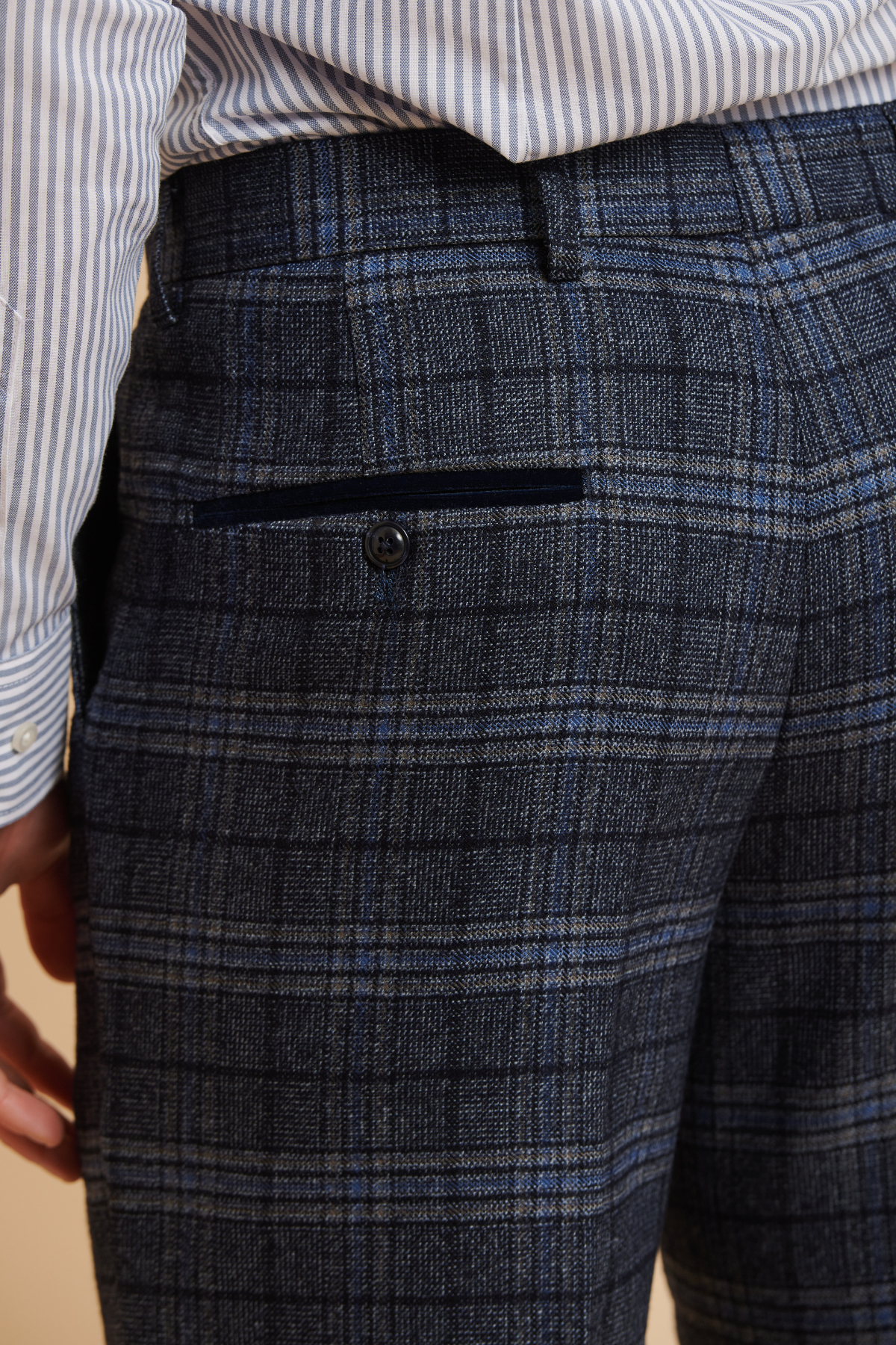 Close-up of a person wearing Marc Darcy's ANDY Blue Check Trousers, featuring a slim fit and buttoned back pocket, paired with a blue and white striped shirt for a polished formalwear look.