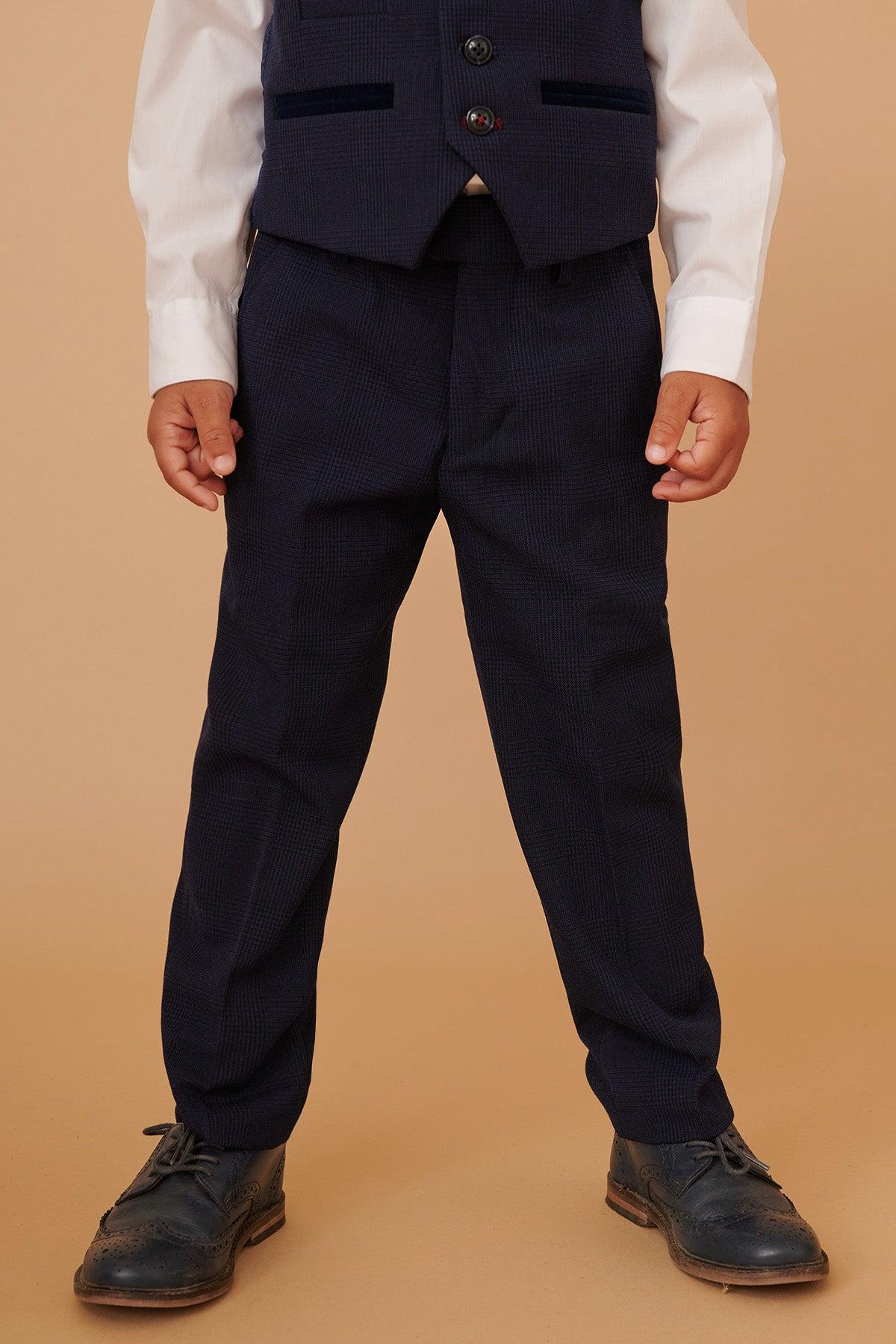A boy wears the Marc Darcy BROMLEY children's navy check print three piece suit—trousers and a matching waistcoat over a white shirt, styled with dark brogue shoes, against a beige background.