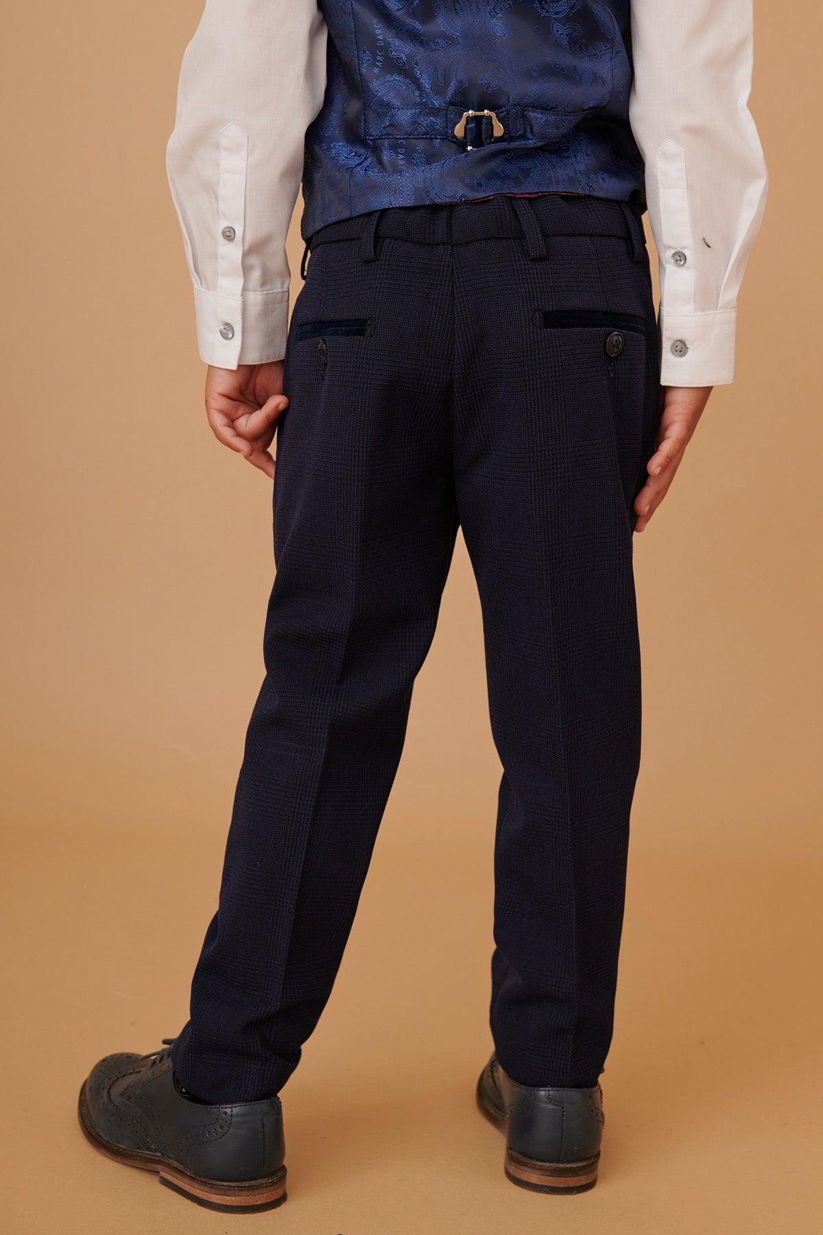 A child wearing the Marc Darcy BROMLEY Childrens Navy Check Print Three Piece Suit, featuring adjustable trousers, a white shirt, blue check vest, and dark shoes, is seen from the back against a beige background.