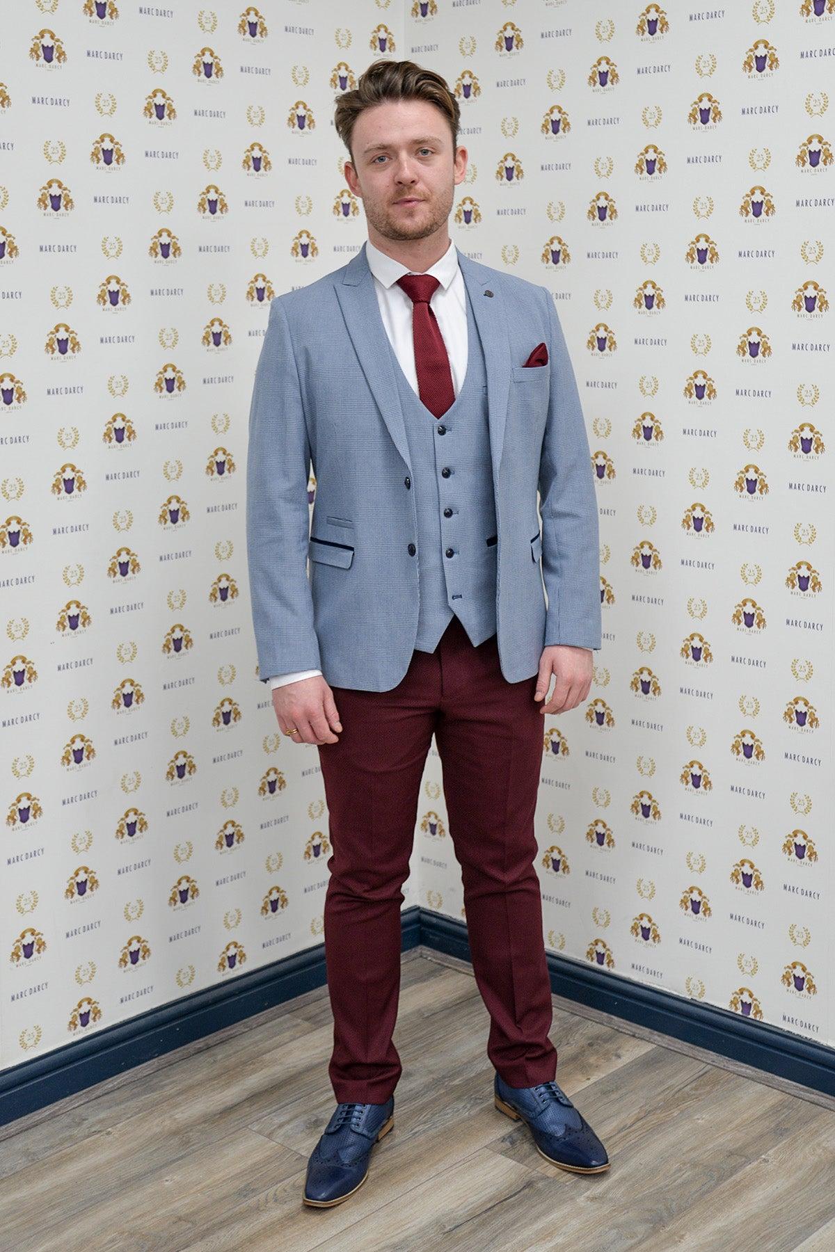 Coronation Street’s Joel Deering (Calum Lill) wears the Marc Darcy BROMLEY Sky Blue Blazer with wine chinos, posing before a backdrop adorned with the Marc Darcy logo.