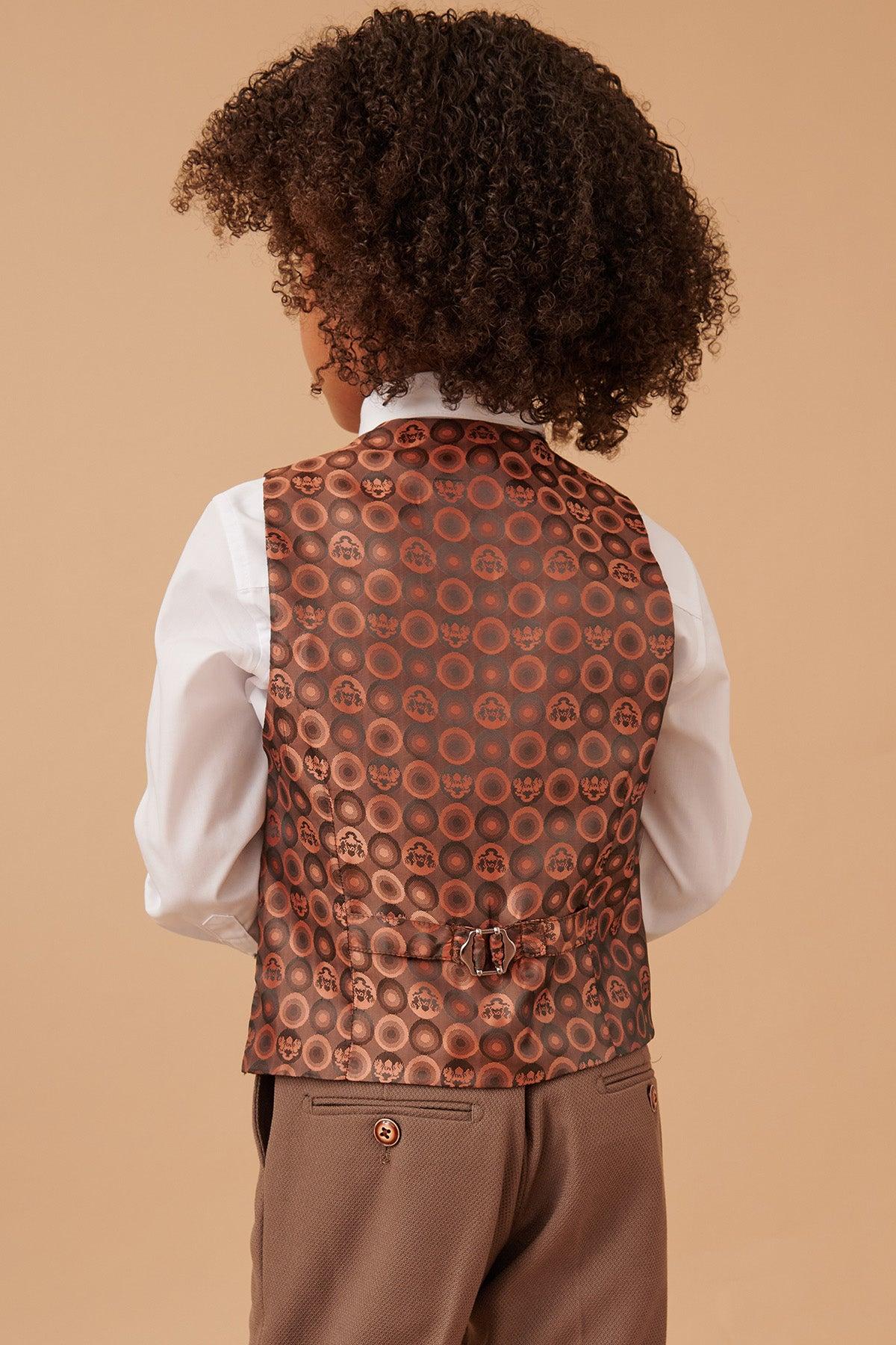 A child with curly hair wears the Marc Darcy HM5 - Childrens Tan Tailored Three Piece Suit, featuring a white shirt, patterned brown vest, and trousers in premium tan fabric, set against a plain beige background.