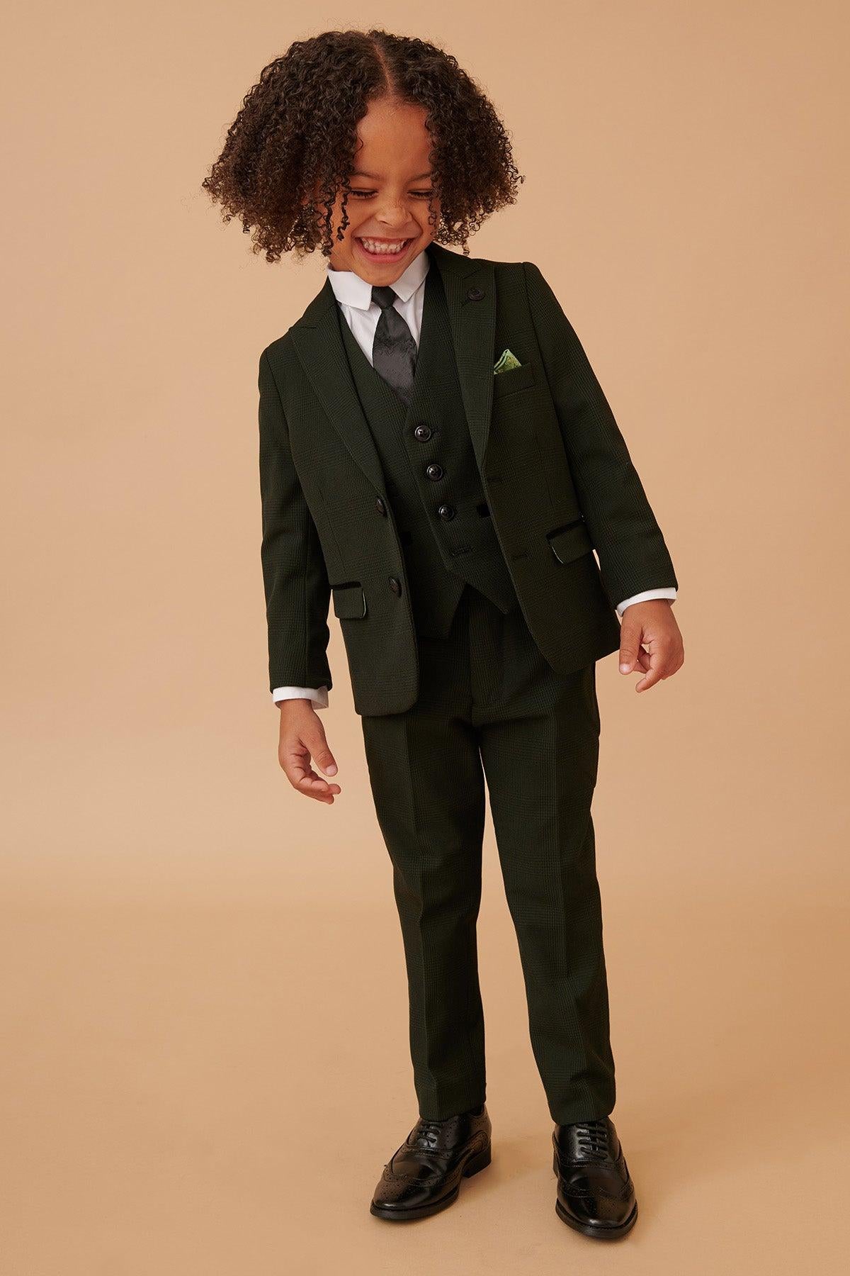 A young boy laughs while wearing the Marc Darcy BROMLEY Children's Olive Green Check Print Three Piece Suit, paired with a white shirt, grey tie, matching vest, and pocket square.